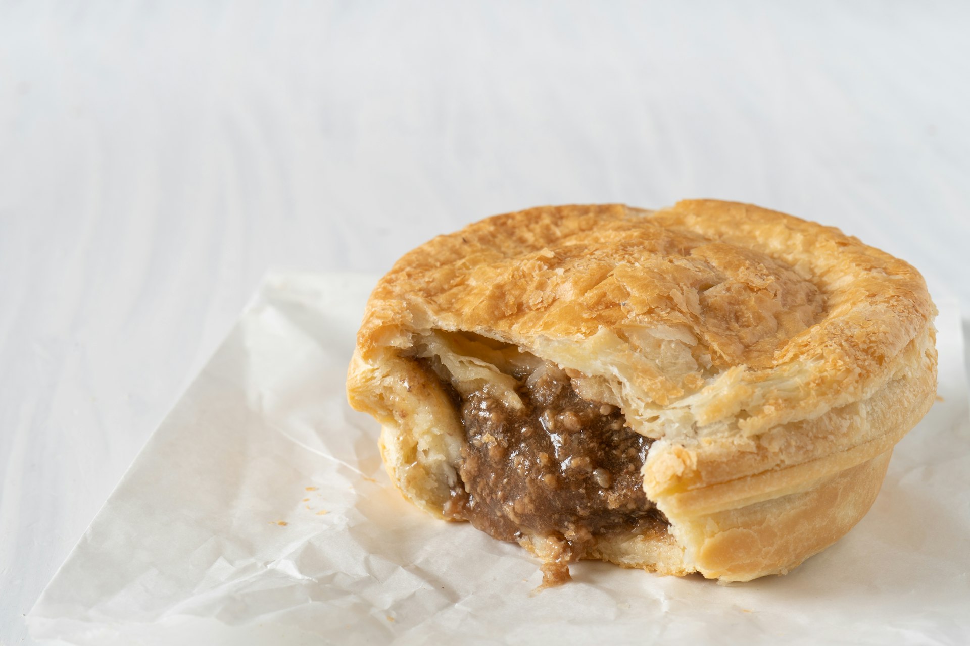 Close-up of a takeaway mince pie with a bite missing on a white paper bag on a white table 