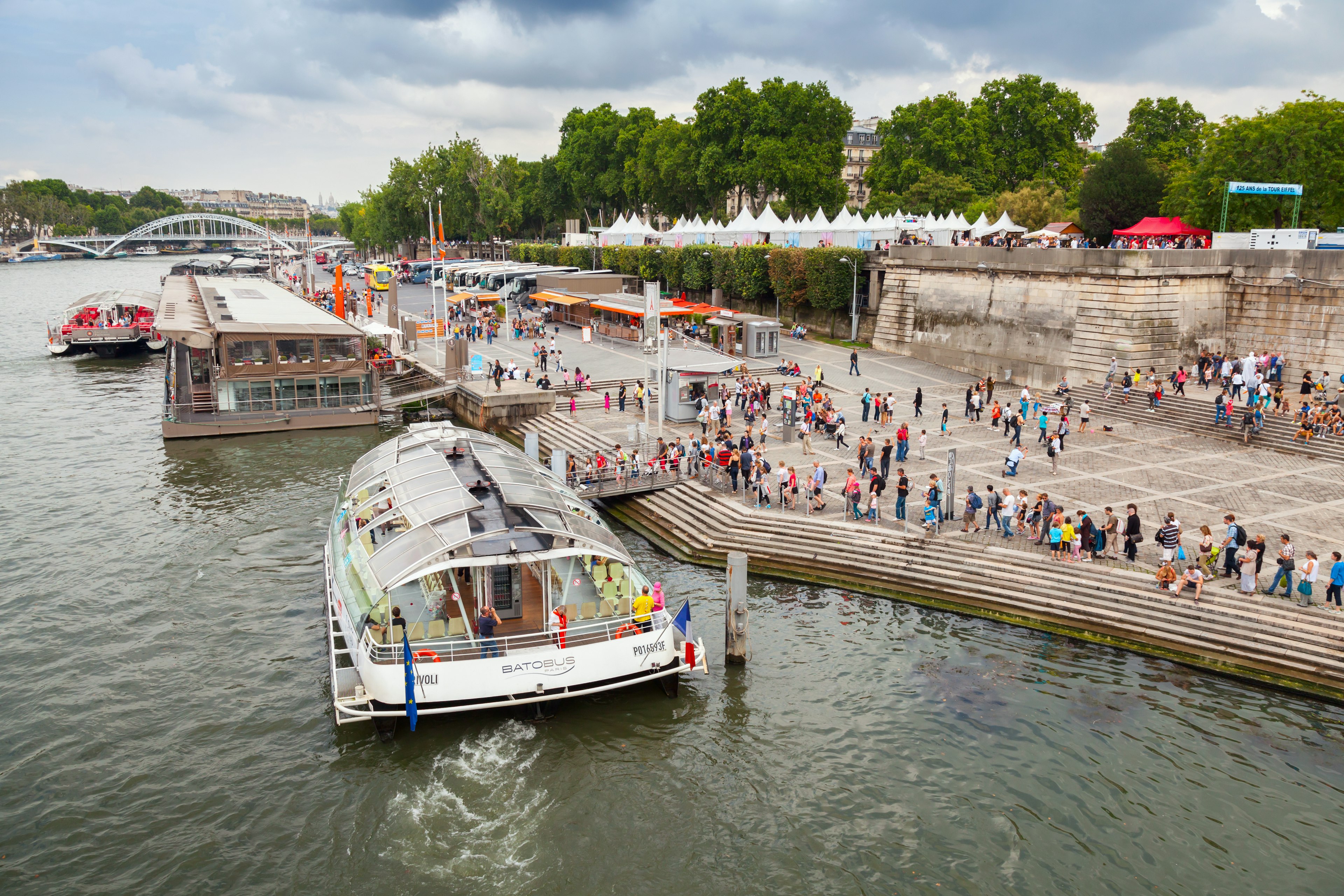 A Batobus boat docks at the side of a river where crowds of tourists are waiting to board