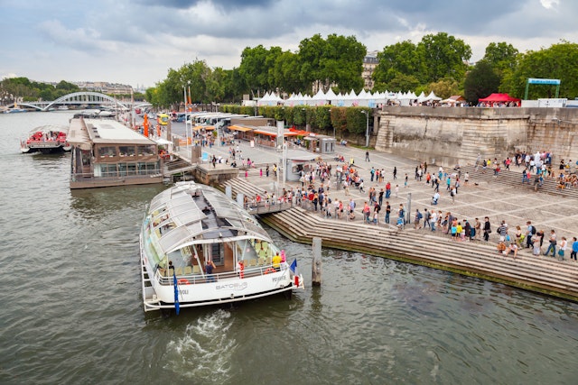 A Batobus boat docks at the side of a river where crowds of tourists are waiting to board