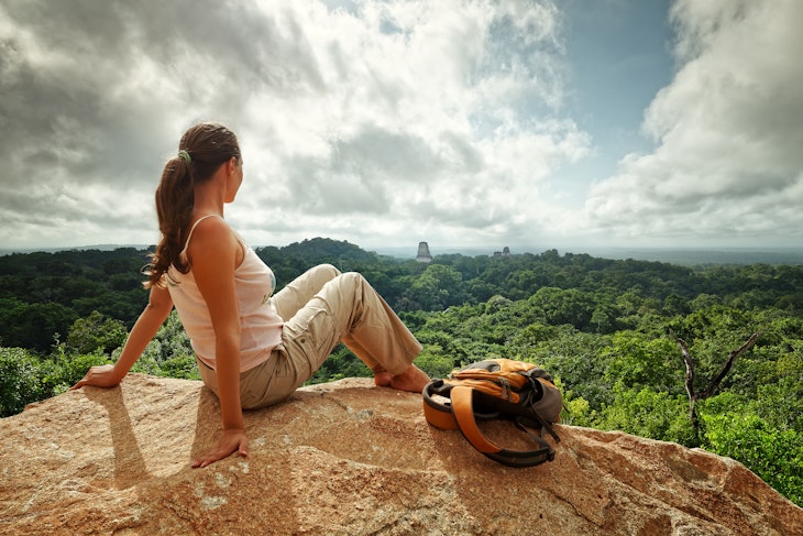 A young woman with a backpack is looking at the ruins of the ancient Maya city, Tikal, in Guatemala