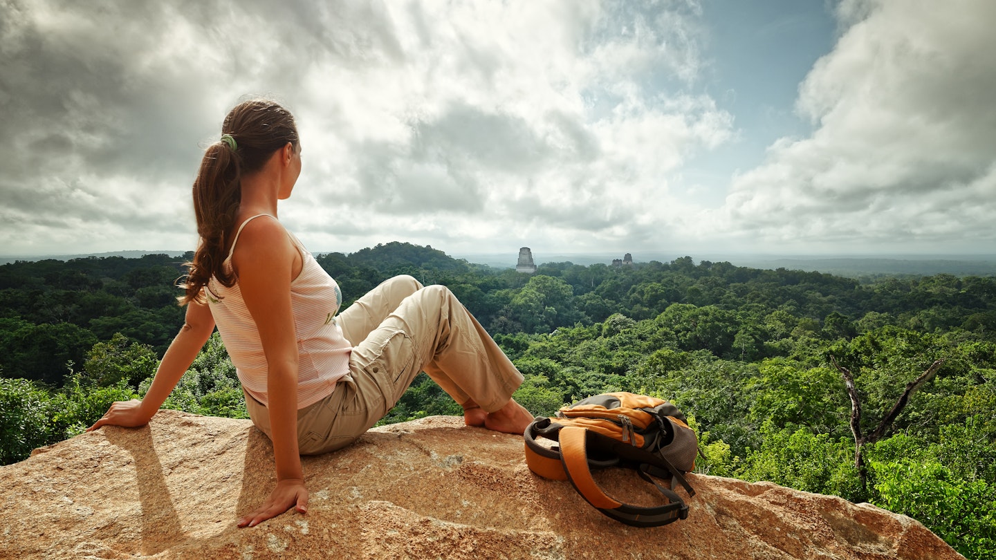 A young woman with a backpack is looking at the ruins of the ancient Maya city, Tikal, in Guatemala