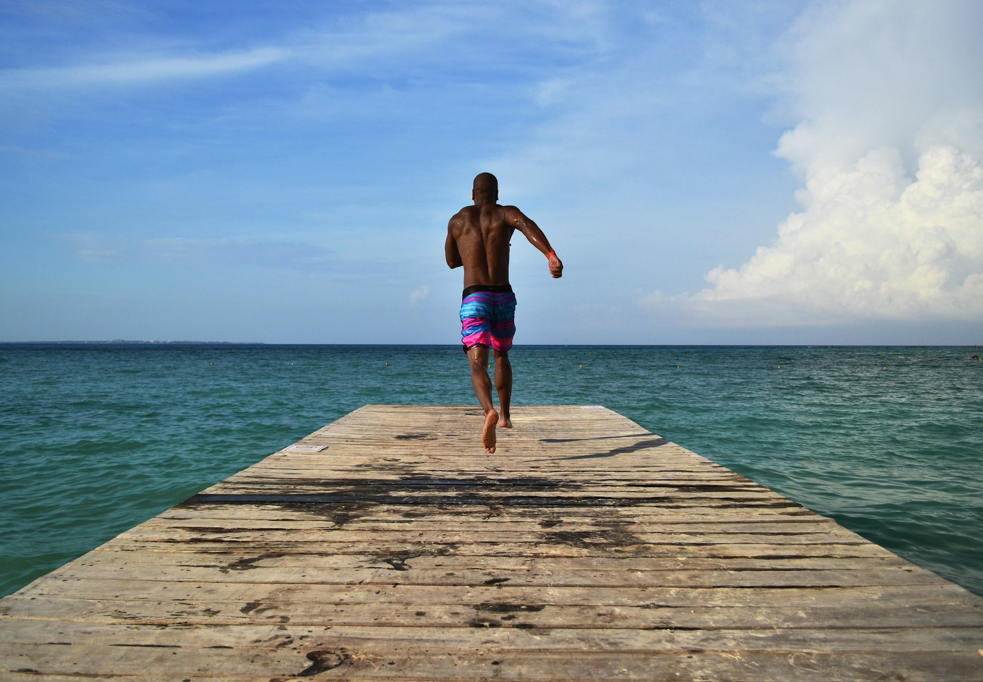 A man runs down a dock to jump in the clear Caribbean ocean in Cancún