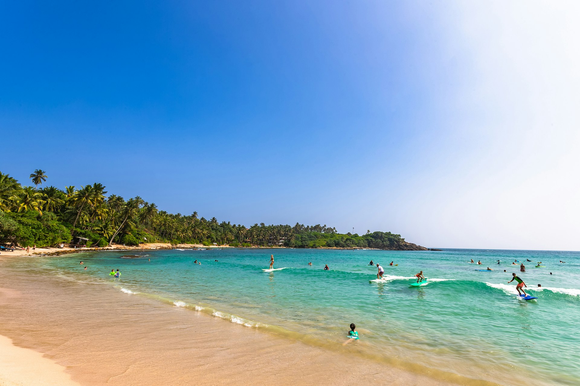 People riding waves at surf beach in Hiriketiya, Dikwella, Sri Lanka.