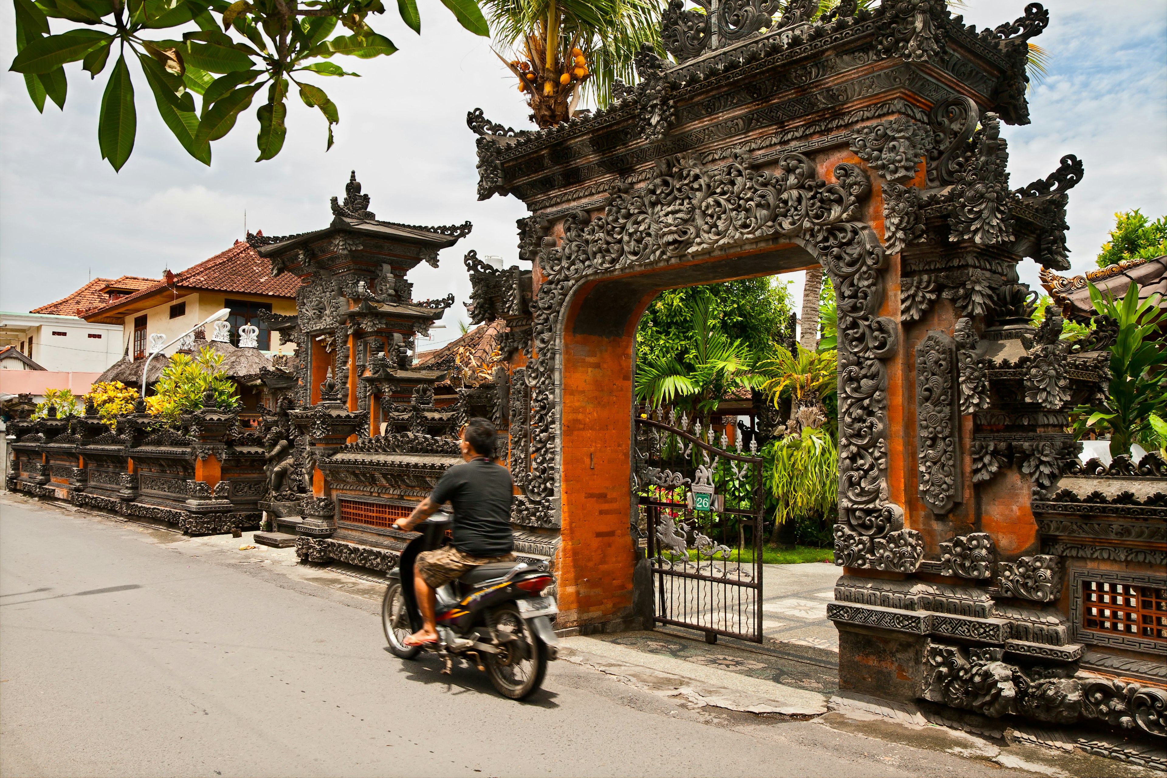 A man rides a scooter past the gates of a Balinese temple