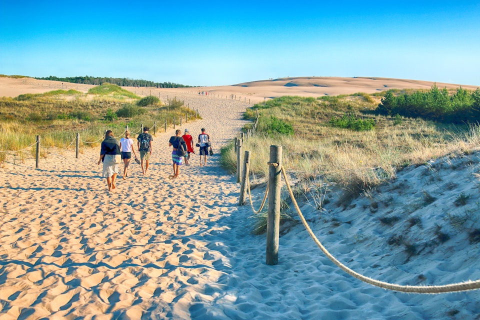 JULY 25, 2019: Visitors walk on a sandy path through sand dunes in the Slowinski National Park on the Baltic Sea coast.
1472037806
attraction, awesome, baltic, beach, beautiful, blue, clear, coast, day, desert, dune, europe, european, incredible, interest, landmark, landscape, largest, leba, most, mountain, moving, national park, nature, north, place, poland, polish, pomeranian, postcard, region, rowy, sand, sea, sky, slowinski, summer, sun, sunny, tourism, tourist, touristic, travel, trip, visited, visitor, wallpaper, wave