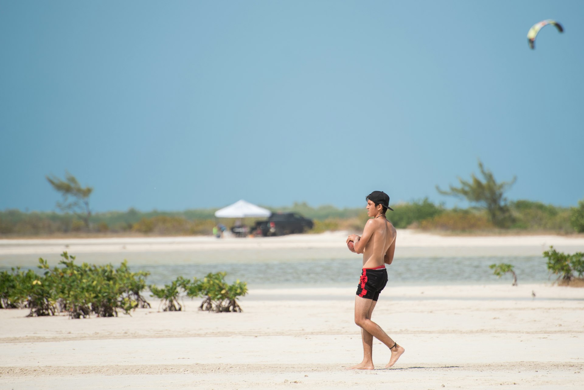 A young man throws a football on a white sand beach at Isla Blanca, Cancún