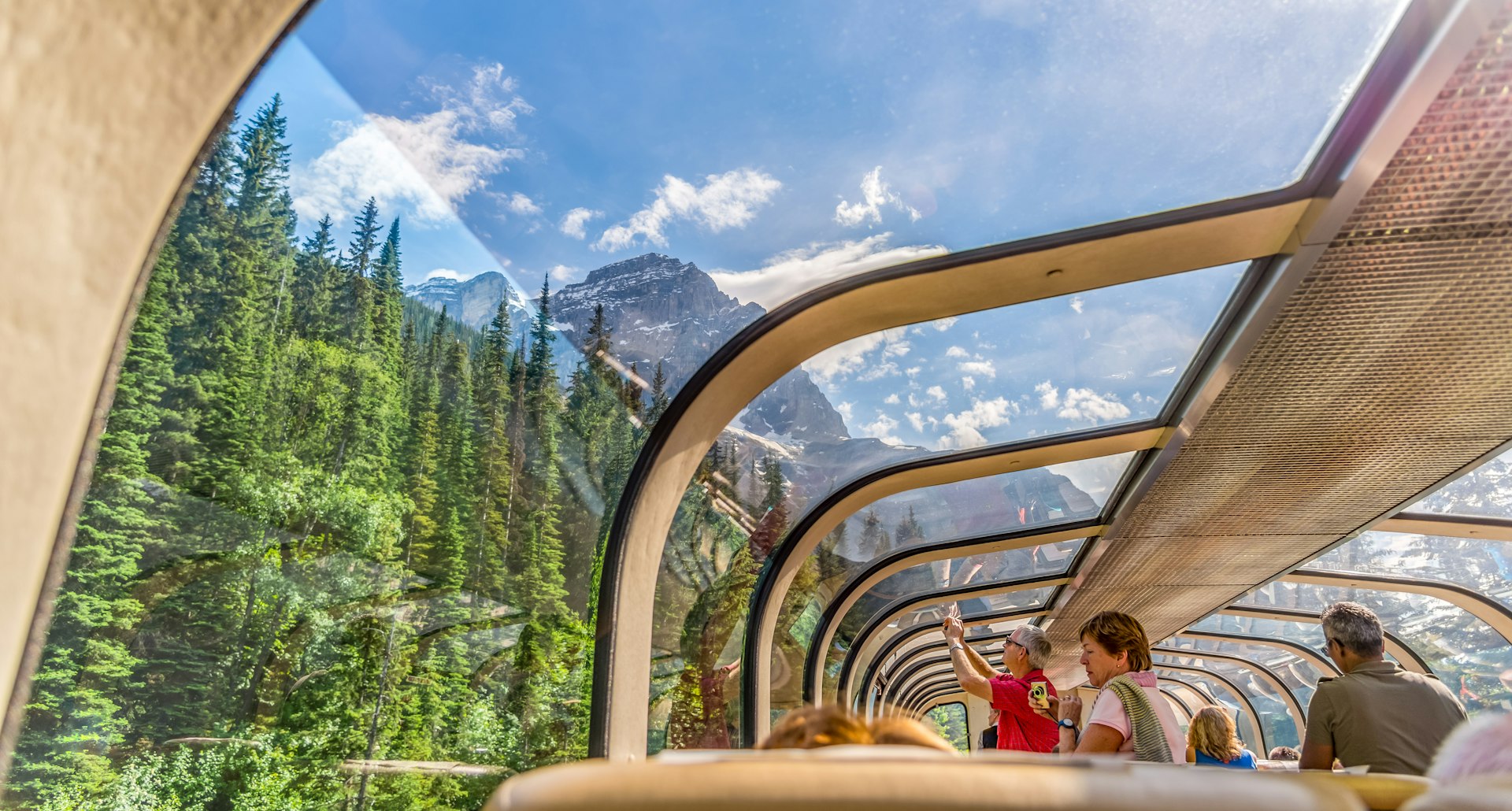 People sit in the observation desk of a train looking out at the Rocky Mountains. 