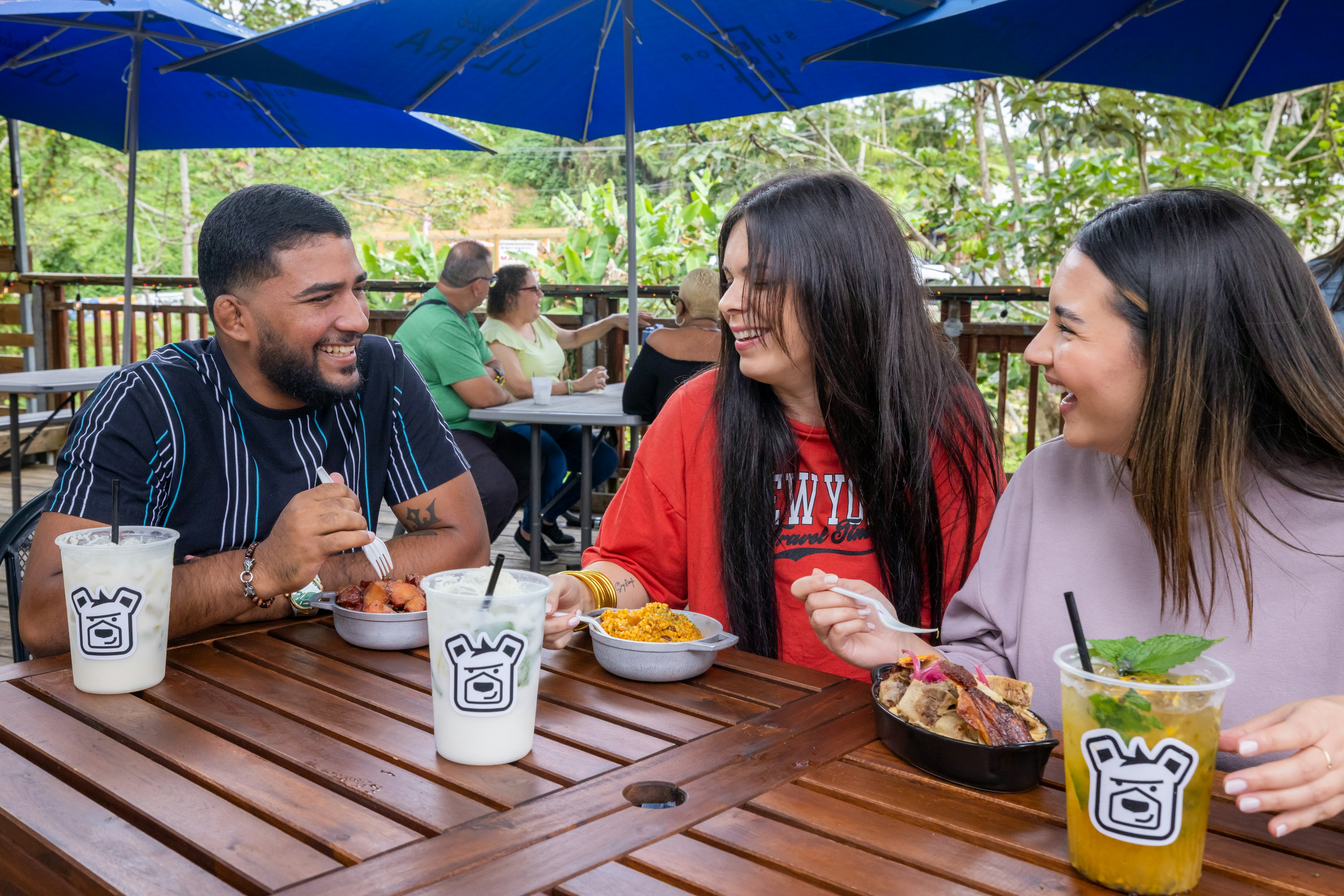 Two women and a man sat at an outside table eating and drinking, Cayey, Puerto Rico