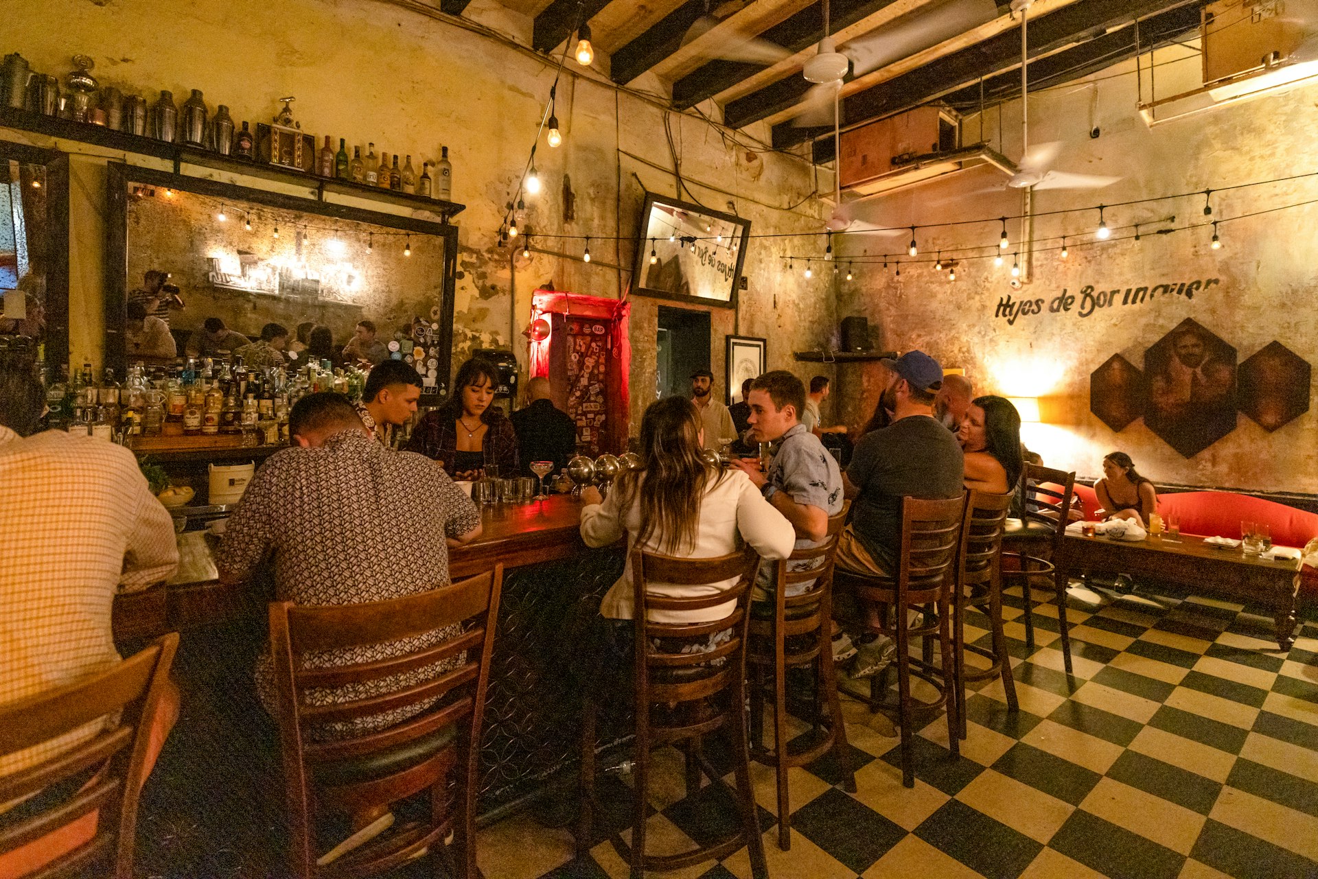 People sit and drink cocktails at La Factoria, Puerto Rico which has a green and white tiled floor and a bar