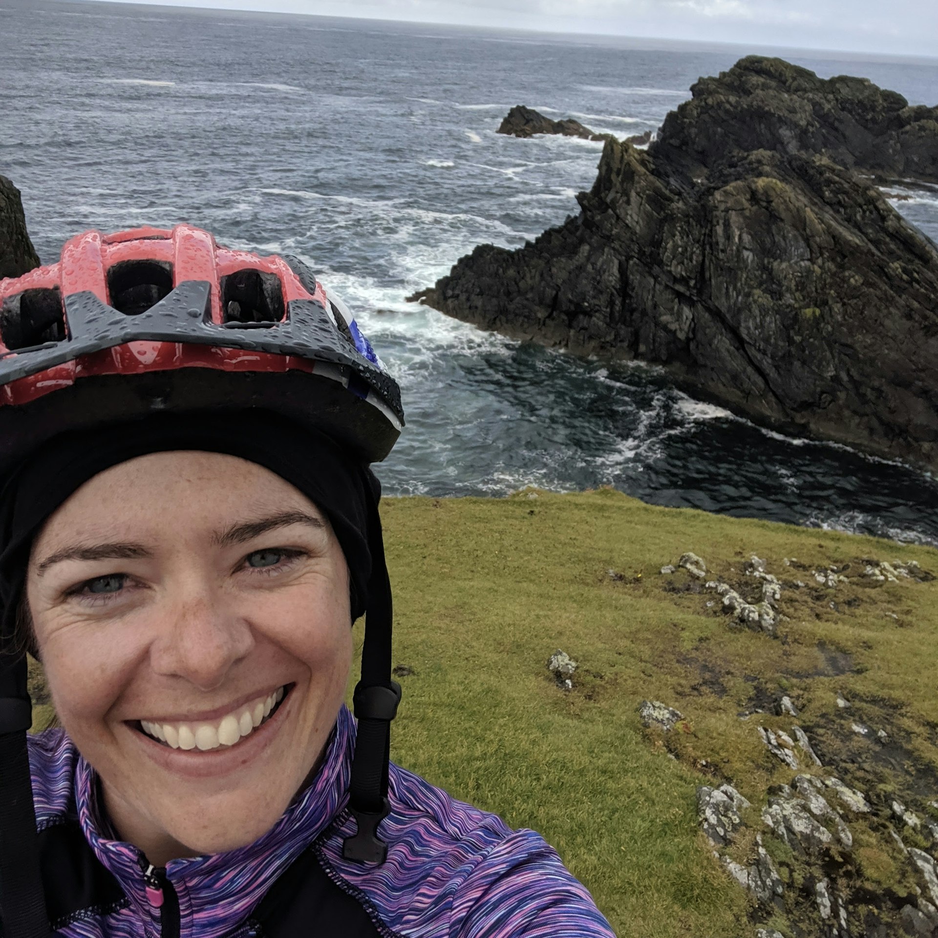 Amy Lynch smiling at the camera with the craggy coastline of the Outer Hebrides, Scotland in the background
