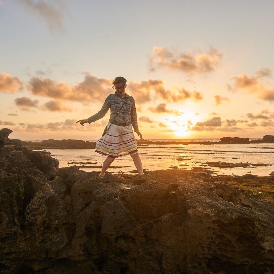 Erin Lenczycki walking on a rocky outcrop along the coastline in Morocco at sunset
