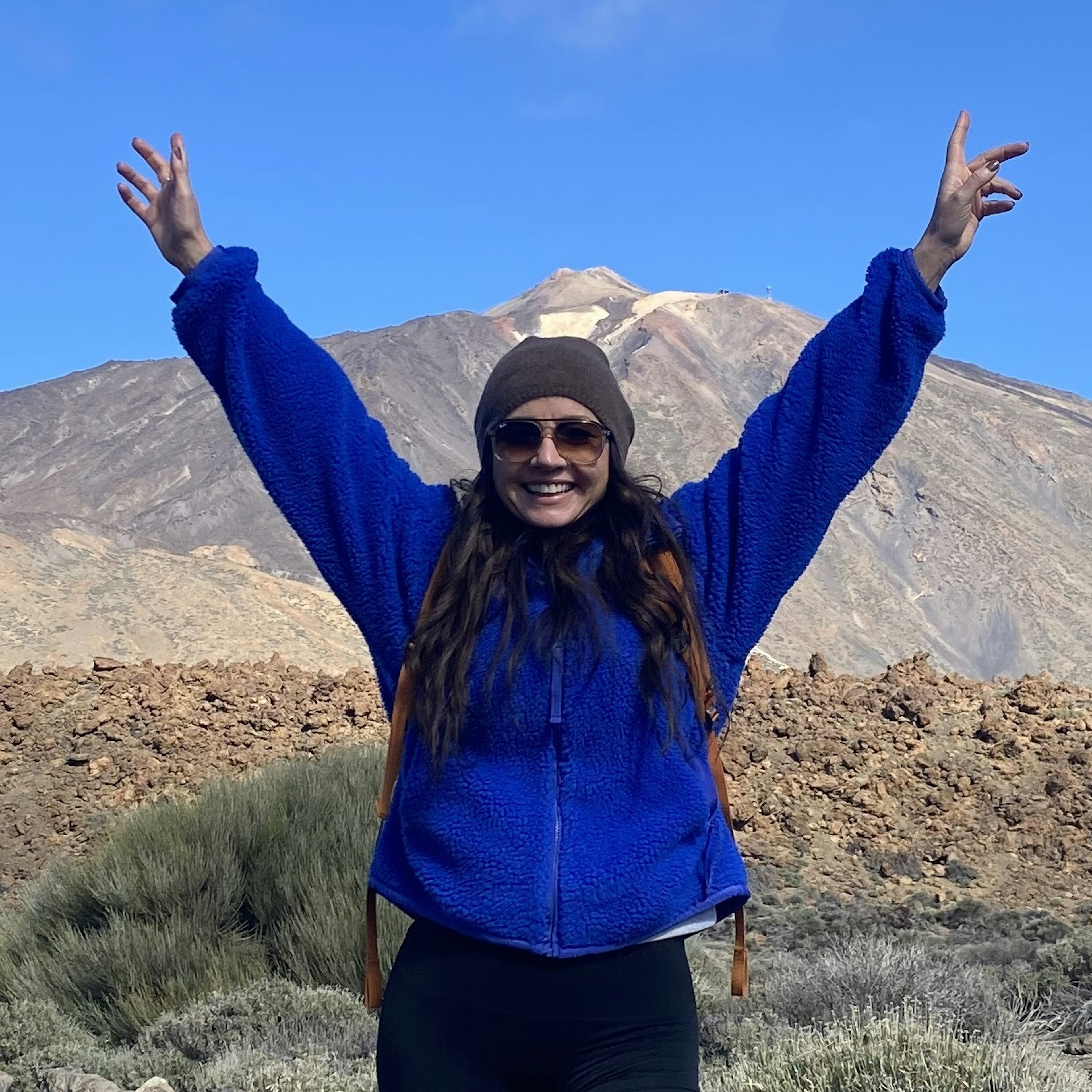 Fionnuala McCarthy stands in front of a huge, snow-topped mountain peak, holding up her arms and smiling