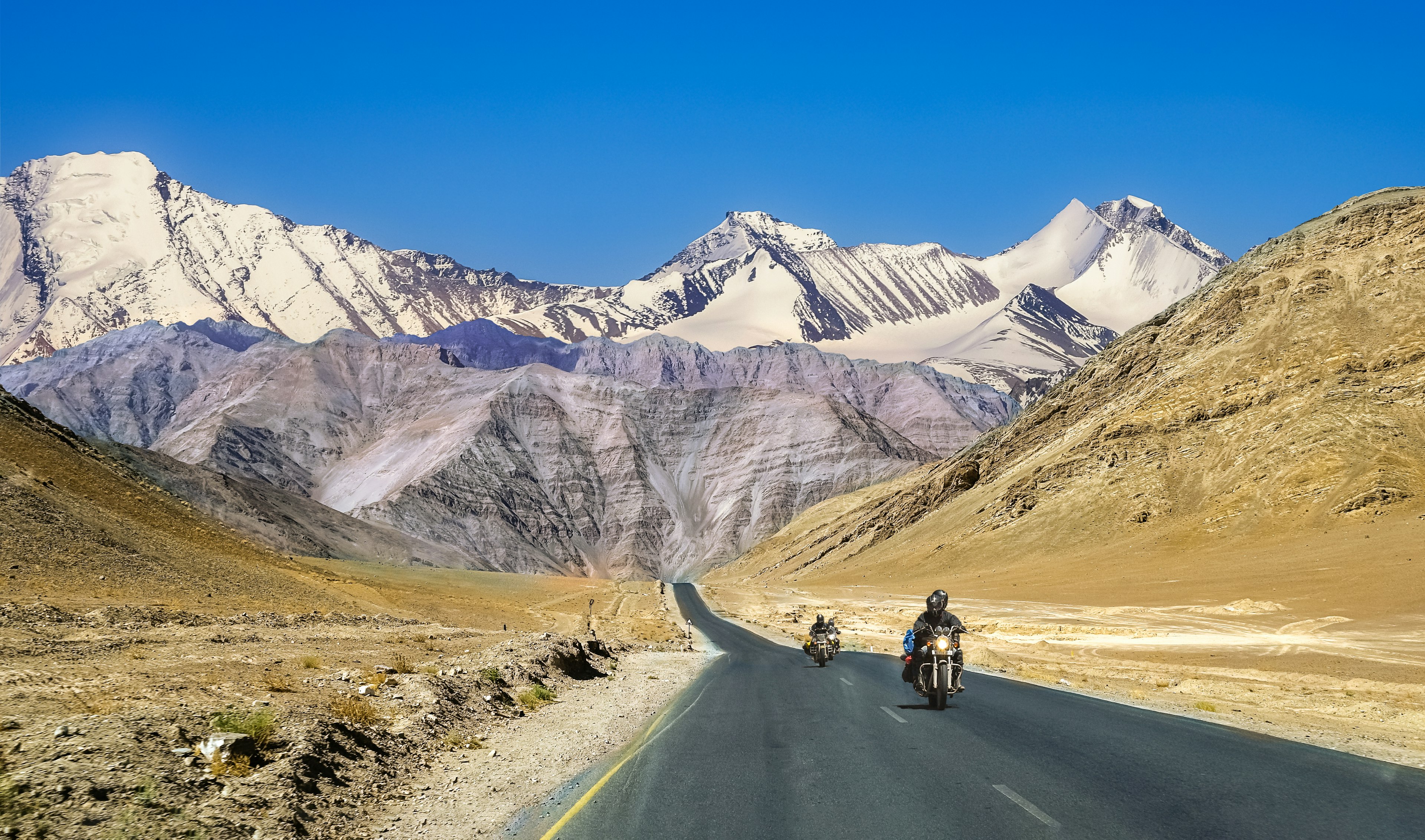 Motorcyclists ride against a mountain backdrop in Ladakh in India.