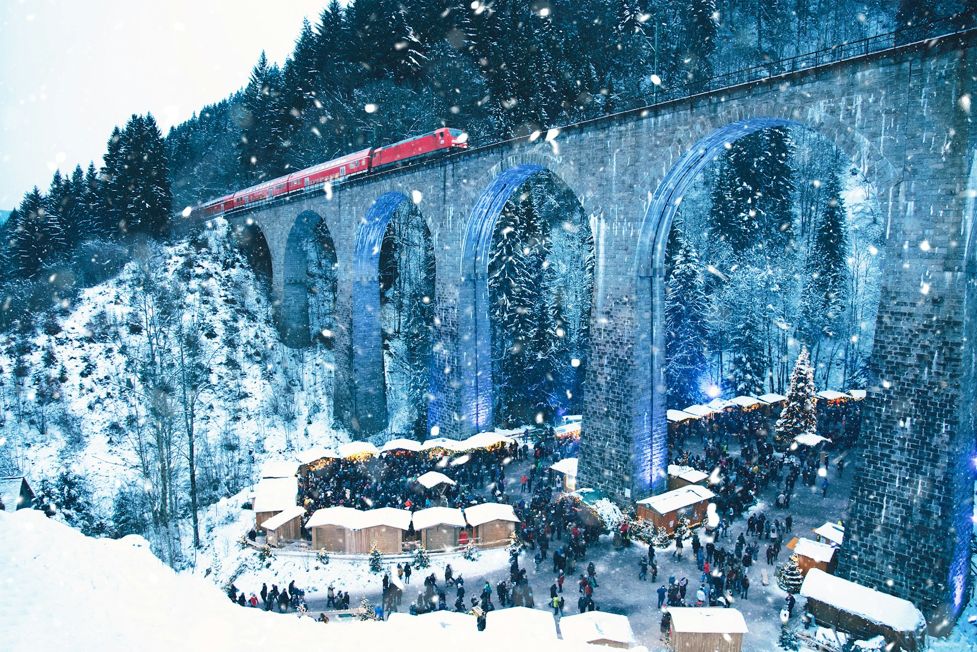 Traditional Christmas market in the Ravenna Gorge, Germany, held under the huge aqueduct with a train passing over it while it's snowing.