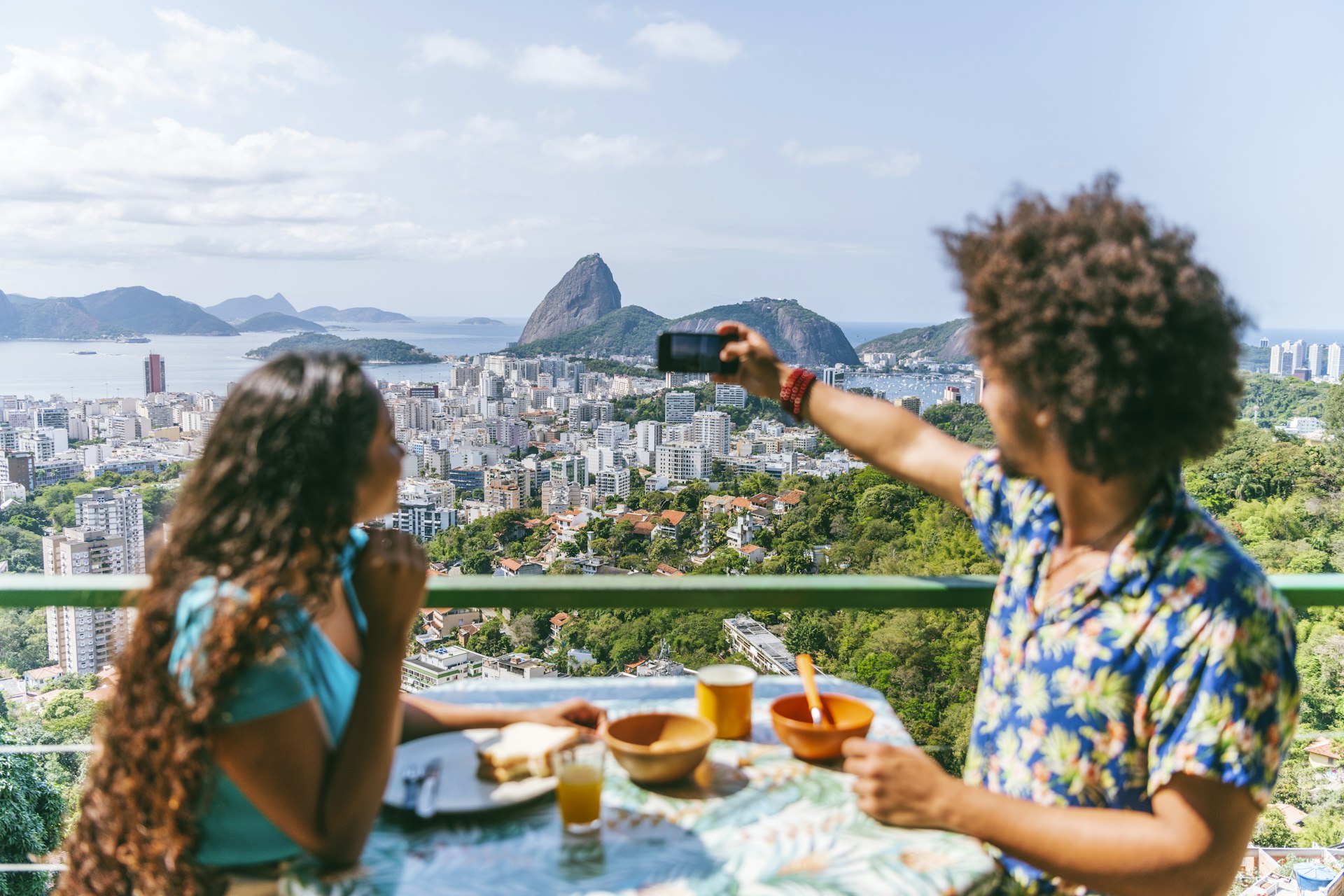 Homem e mulher brasileiros sentados à mesa em um terraço com vista para o Pão de Açúcar, Rio de Janeiro, Brasil (Brasil)