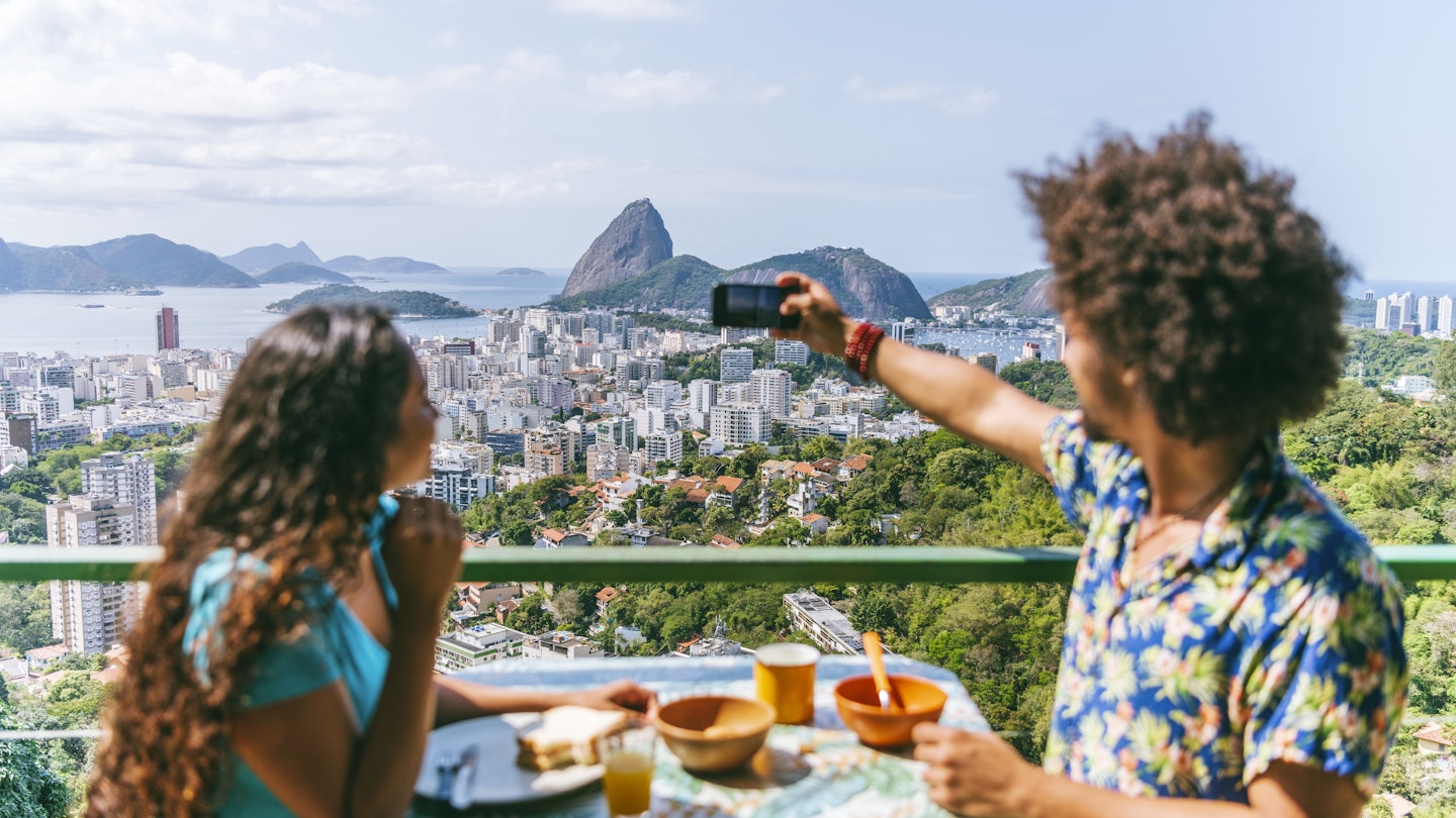 Brazilian man and woman sitting at table on vacation, eating breakfast on terrace, looking away, photographing Sugar Loaf Mountain
1065524330
Couple on hotel balcony with camera phone, Rio de Janeiro - stock photo
Brazilian man and woman sitting at table on vacation, eating breakfast on terrace, looking away, photographing Sugar Loaf Mountain