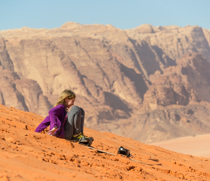 Young girl sliding on sand with a snowboard in Wadi Rum, Jordan.