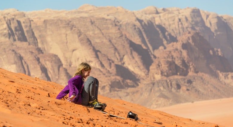 Young girl sliding on sand with a snowboard in Wadi Rum, Jordan.