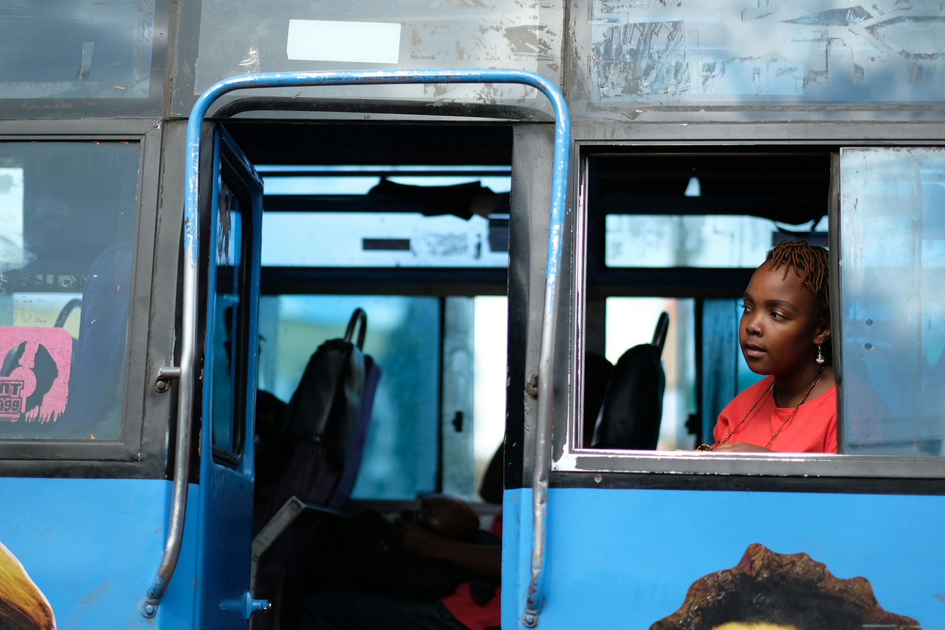 A woman sits in the window seat of a bus looking out ahead at the road