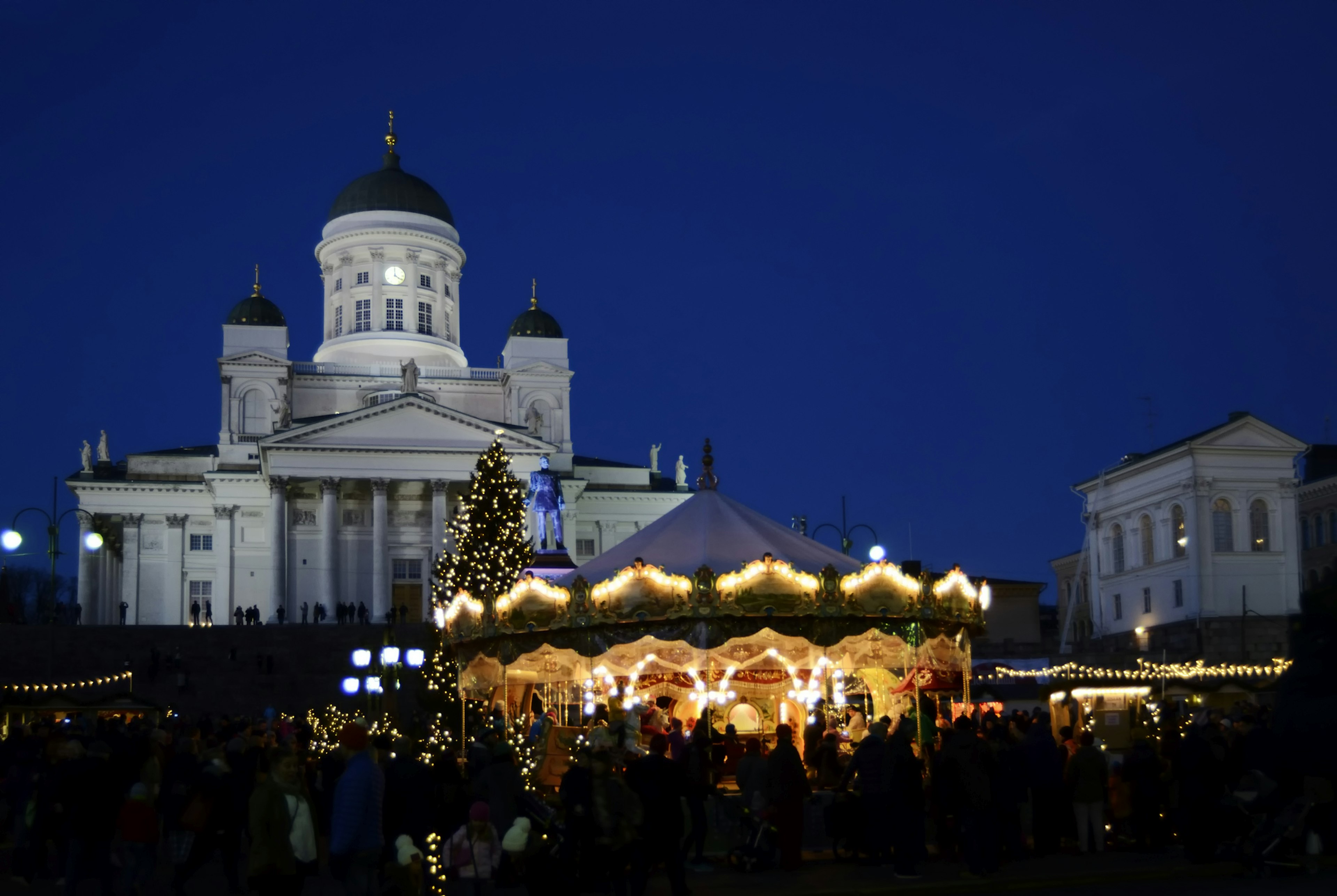 At night, a traditional lit-up carousel at a Christmas market in Helsinki whirls around in front of the church