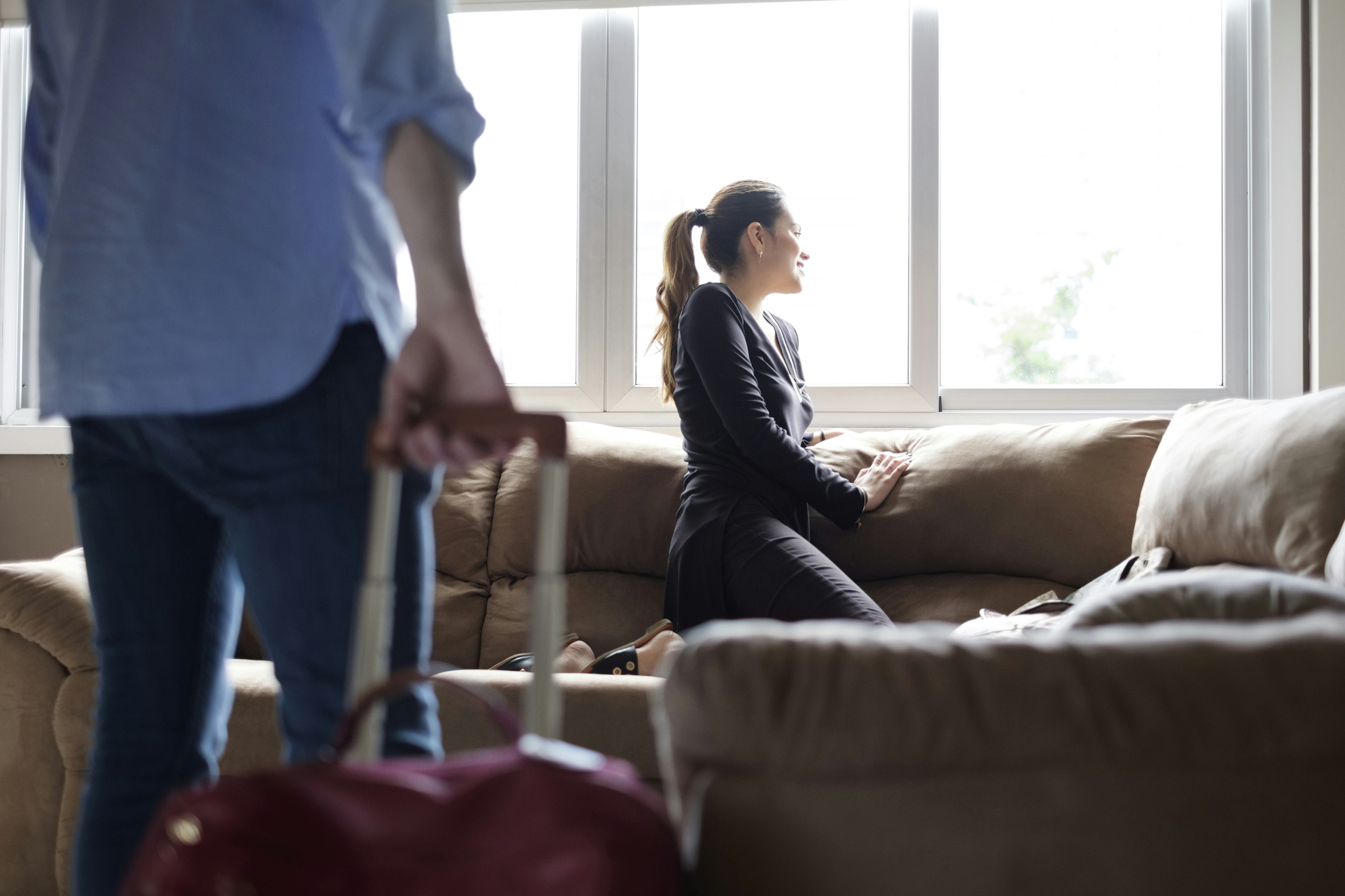 A couple in a larger hotel room in Panama with the woman staring out the window and the man pulling a red suitcase