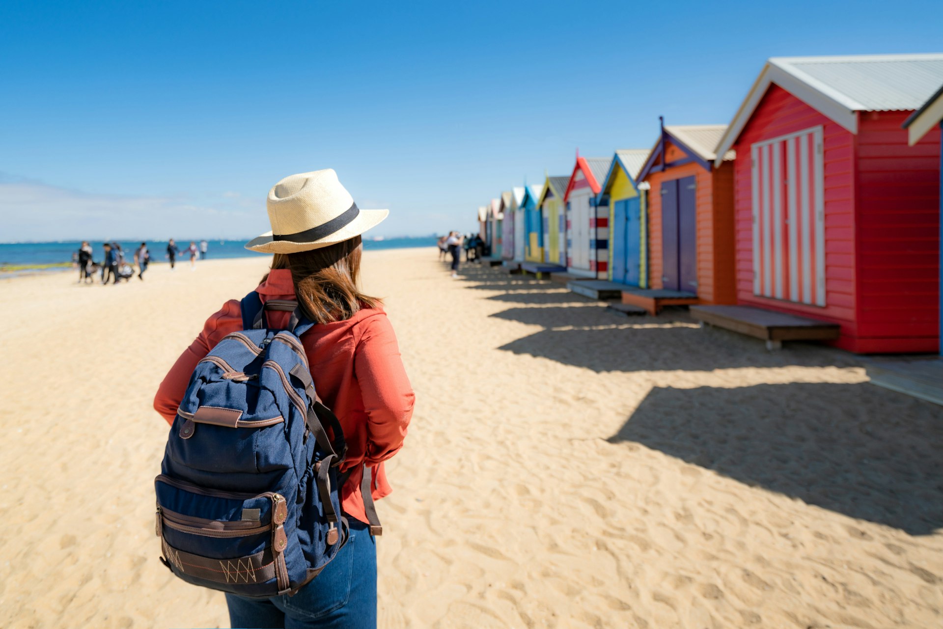 A woman with a backpack looking at the row of bathing boxes on Brighton Beach, Melbourne