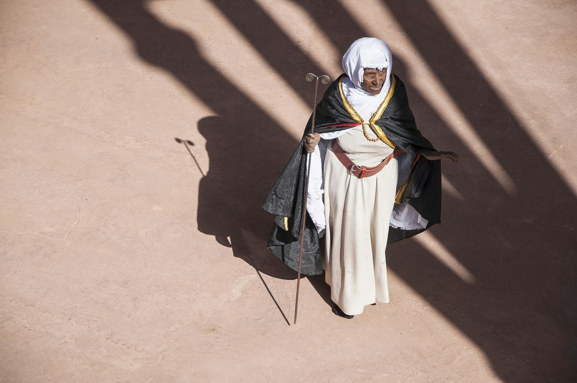 Senior African Christian woman in traditional dress casts a shadow under the sun