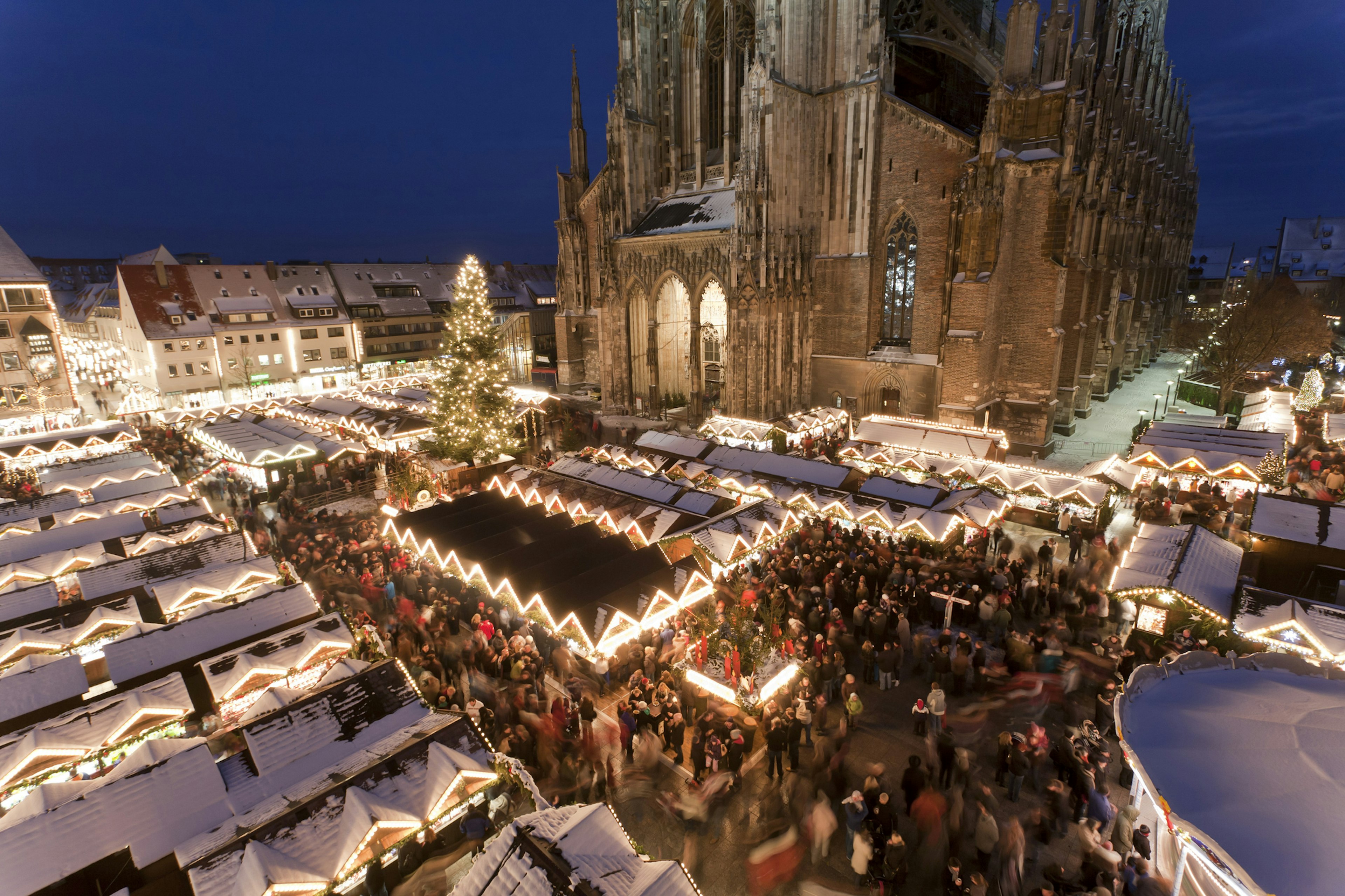 A huge crowd of people at a Christmas market in front of the massive Gothic cathedral at nighttime