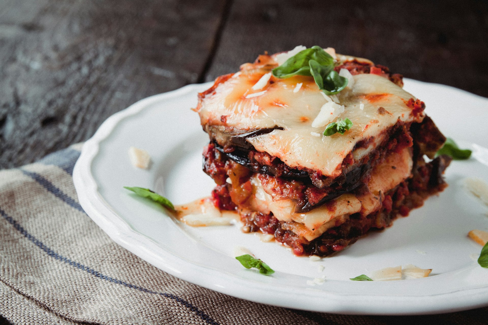 traditional Parmigiana di melanzane: baked eggplant - italy, Sicily cuisine.Baked eggplant with cheese, tomatoes and spices on a white plate. A dish of eggplant is on a wooden table