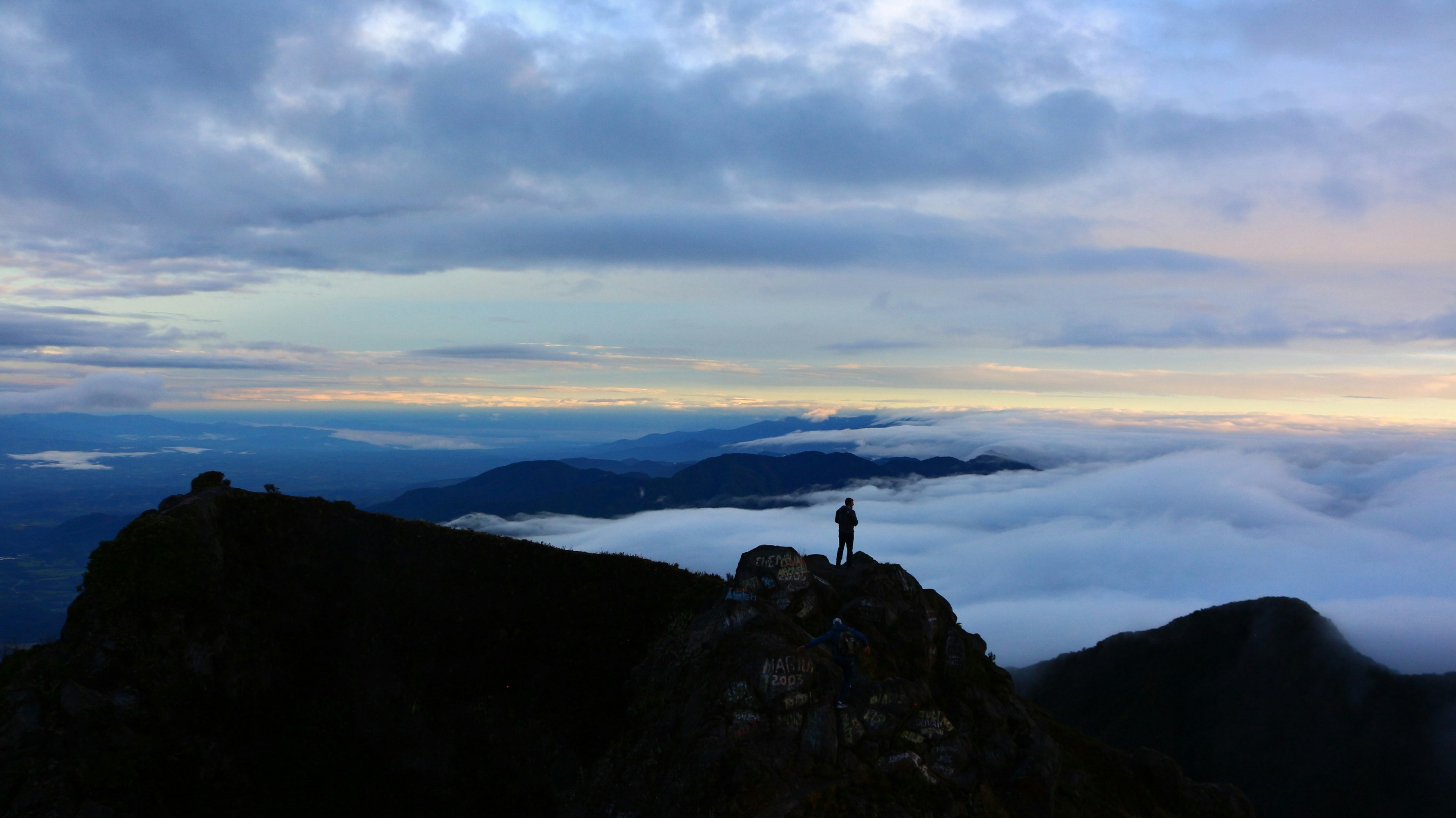 A solo figure stands at the top of a volcano as the sun rises