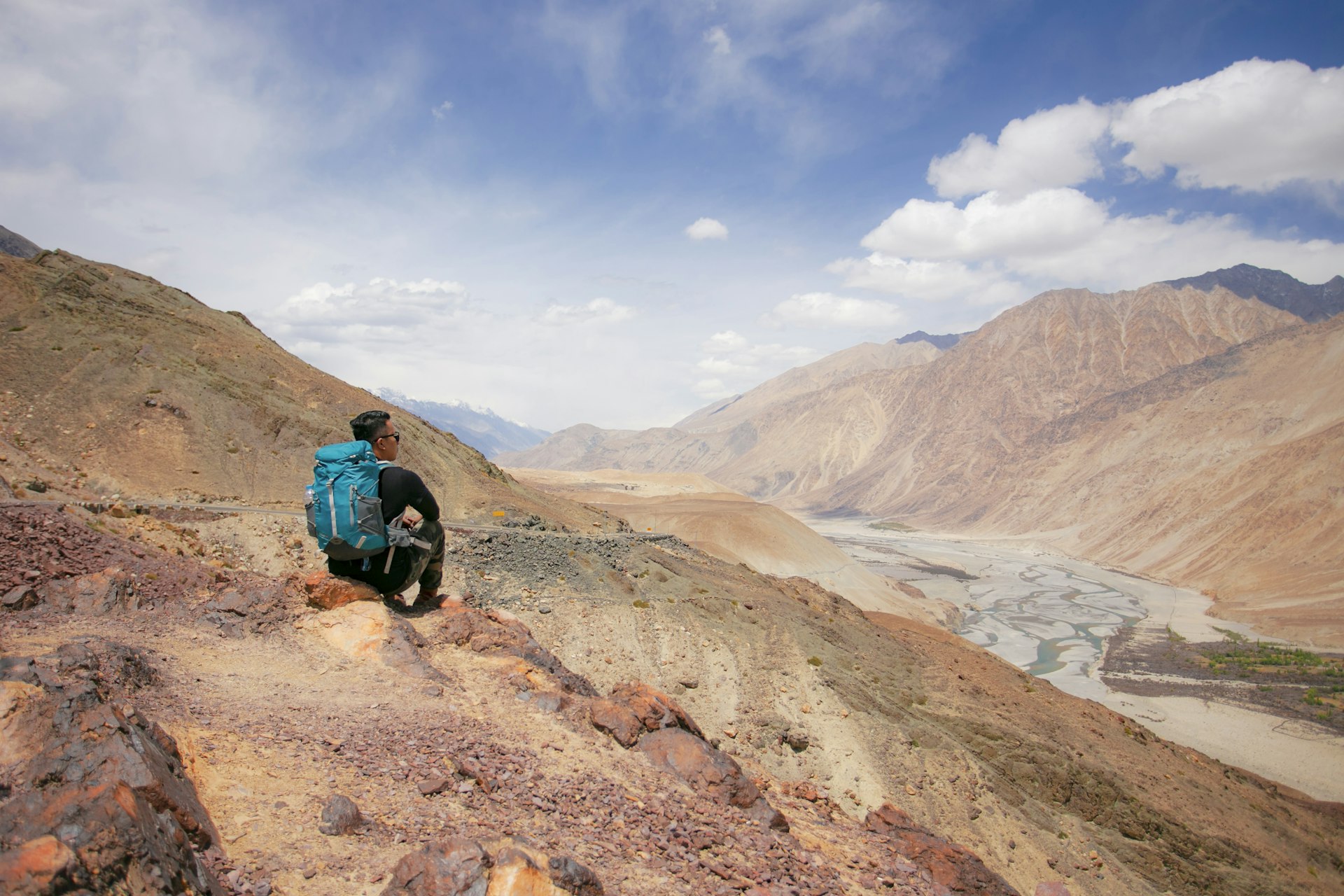 A man sits on the side of a red rock mountain in the Indian Himalayas