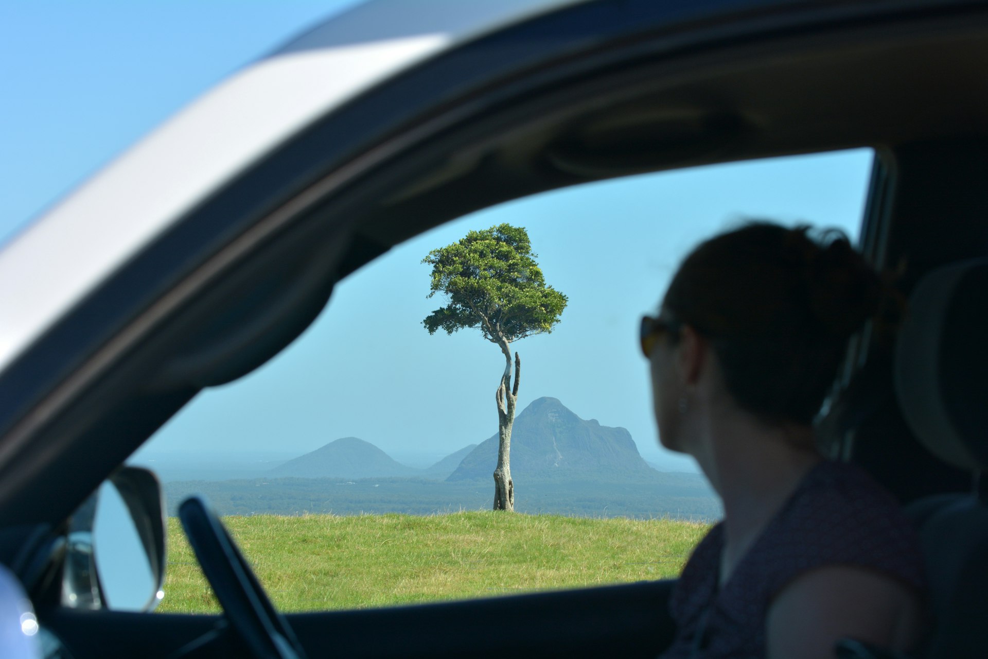 Silhouette of adult woman looking from a car window at Glass House Mountains, a popular tourist destination in the Sunshine Coast in Queensland, Australia