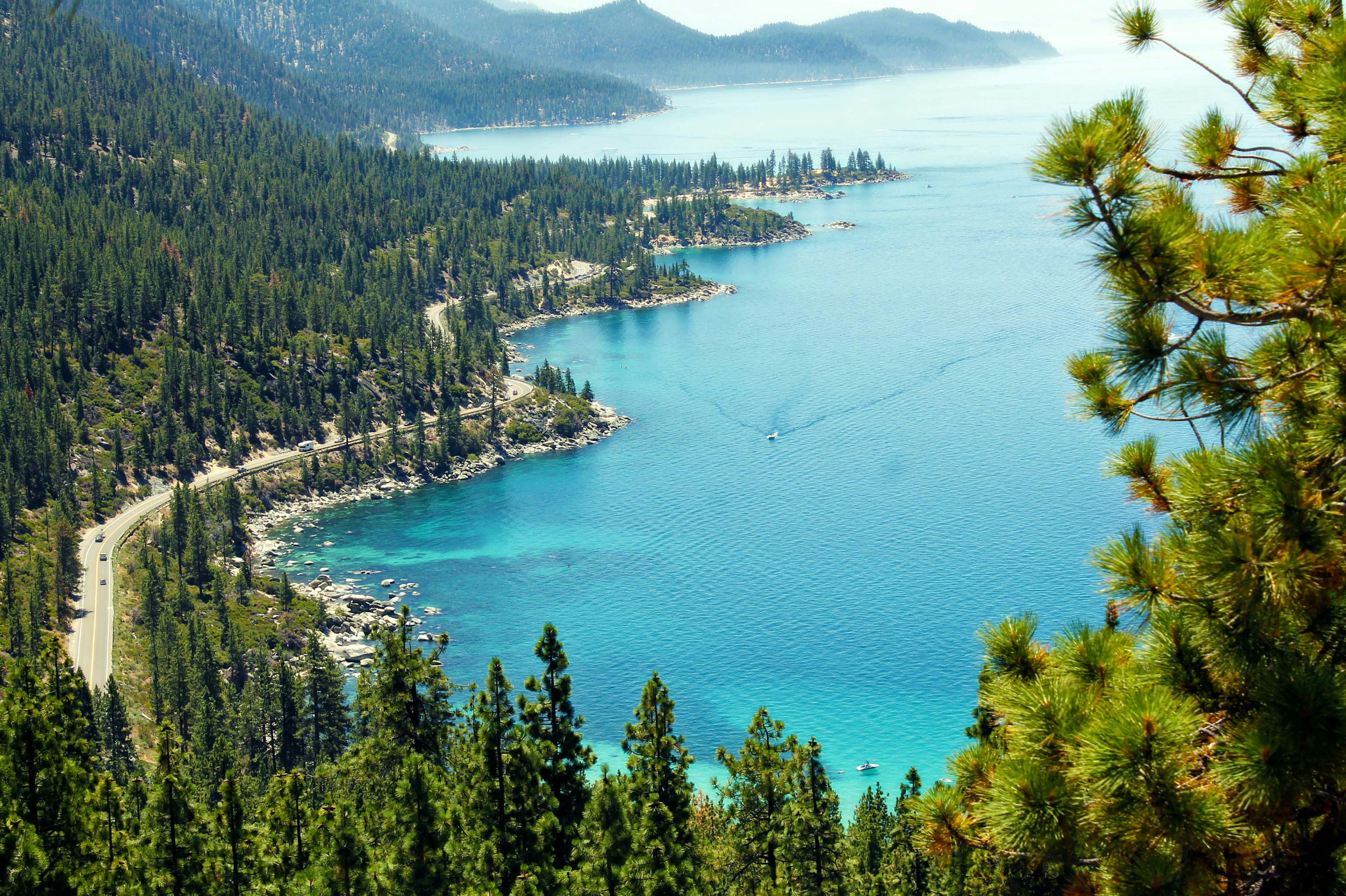 A boat travels along a sparkling lake with a road running alongside it