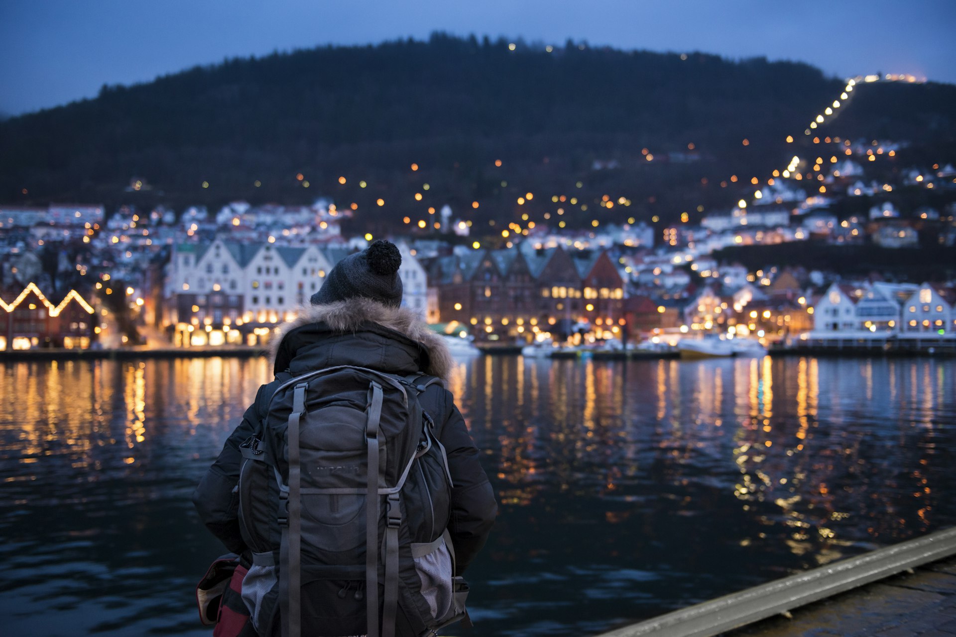 A man in a parka stands in front of the harbor at night, Bergen, Norway