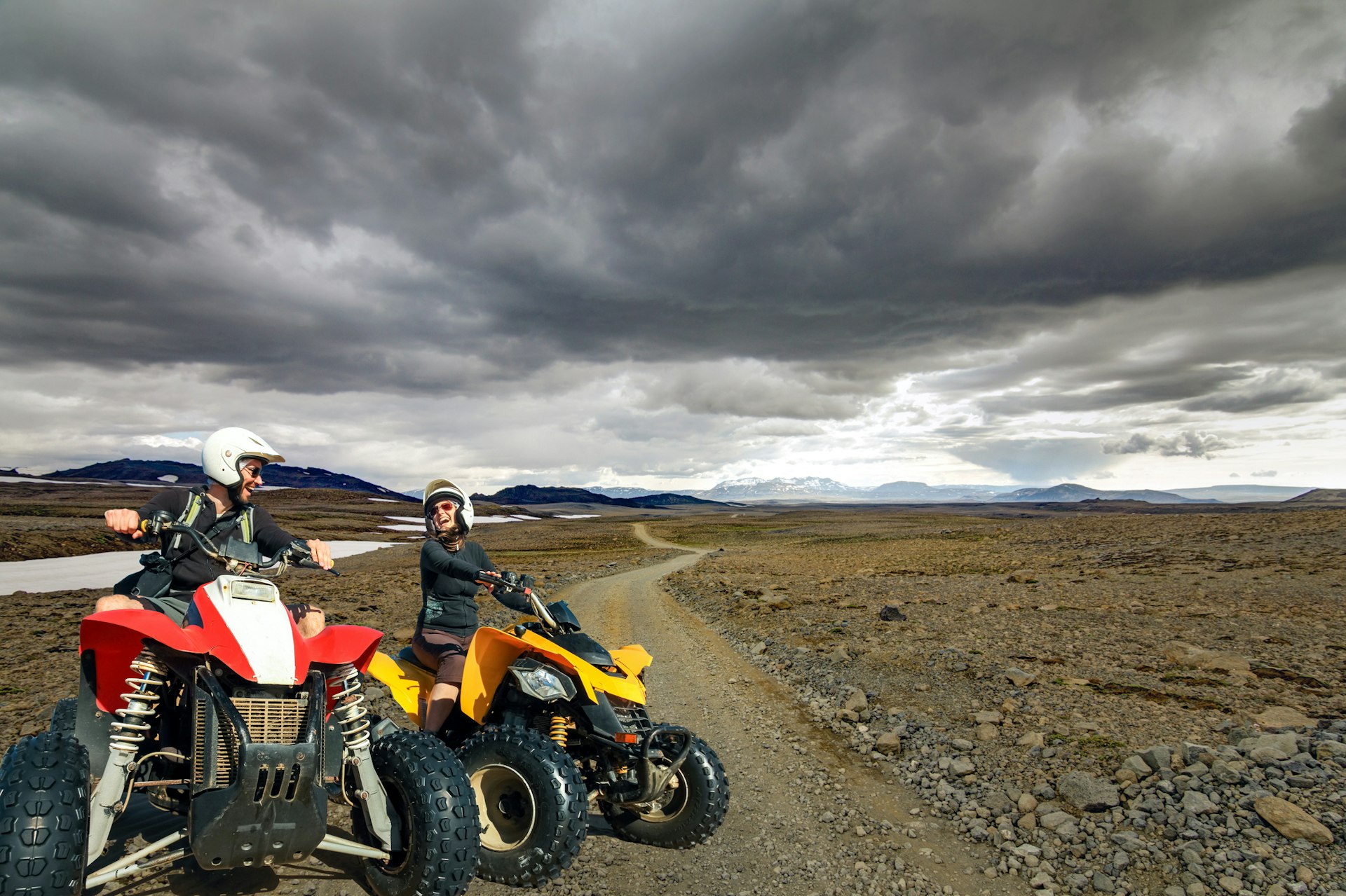 Laughing young couple ATV quad bikers smile joyful, cheerful and driving in icelandic Highland Landscape with quadbikes on dirt road F550 in Kaldidalur, Iceland.