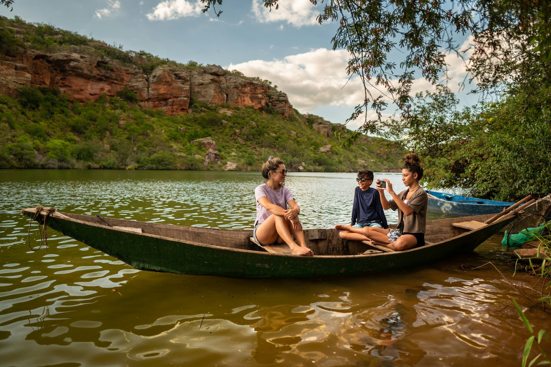Three young teens take photos from a small canoe out on a river