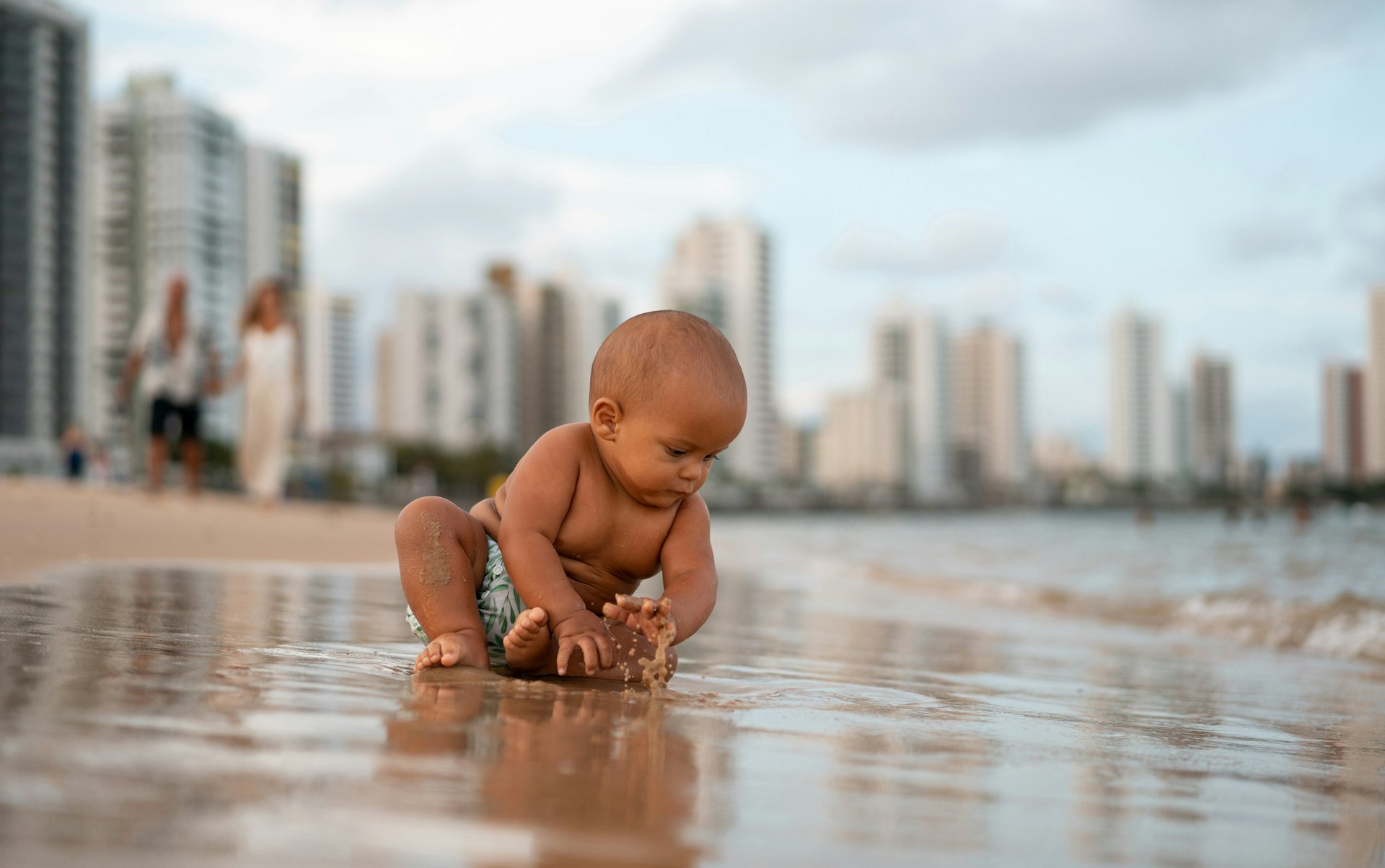 A baby plays on in the sand on the beach in a resort town
