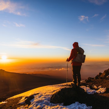 Man with backpack and hiking poles got to the top of Africa - Mount Kilimanjaro and looking at the beautiful bright sunny sunrise above the Meru mountain
1306316004