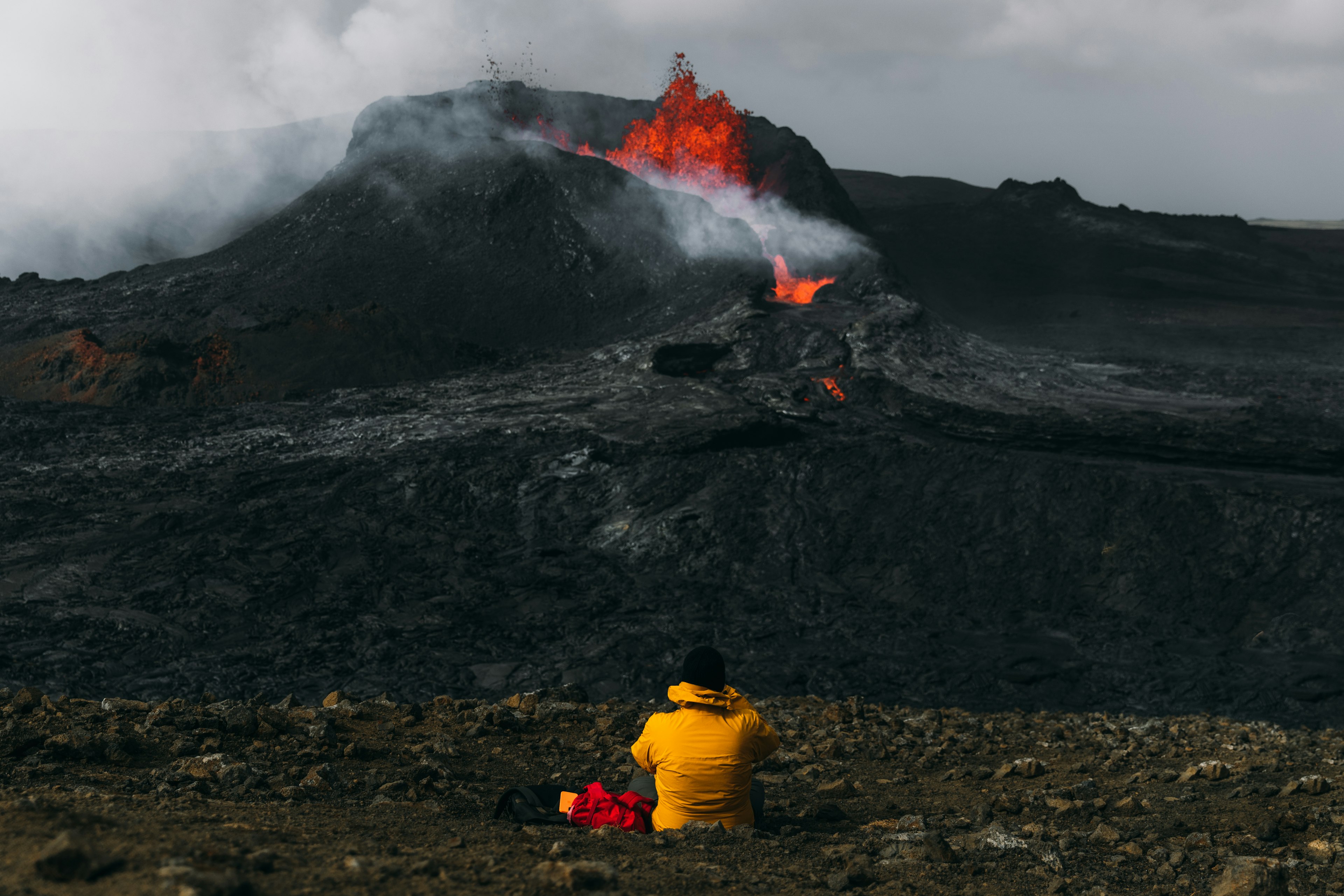 Young man backpacker in yellow jacket watching a volcano erupt, Iceland