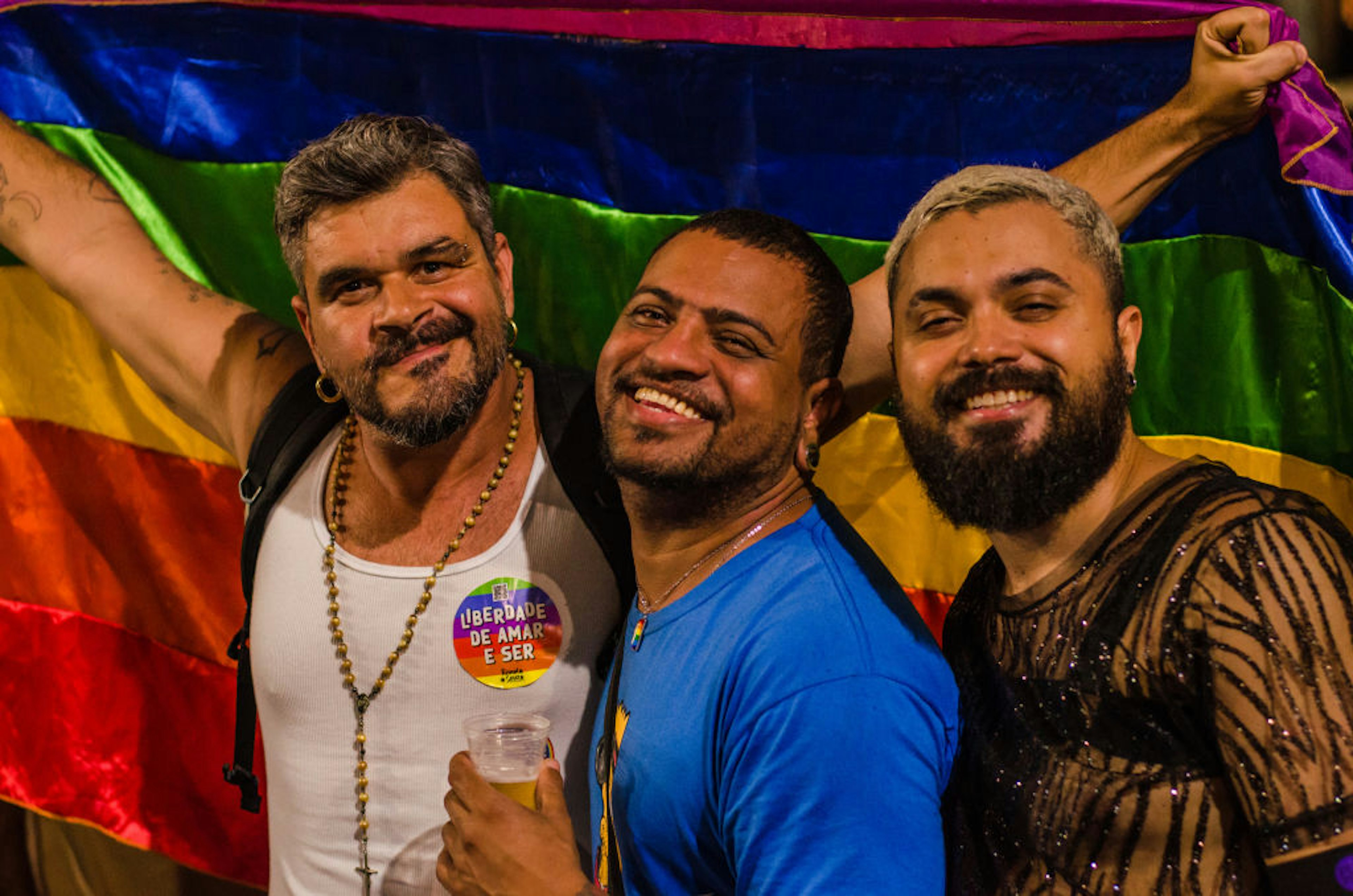 Three men carrying a pride flag and smiling in Rio de Janeiro, Brazil