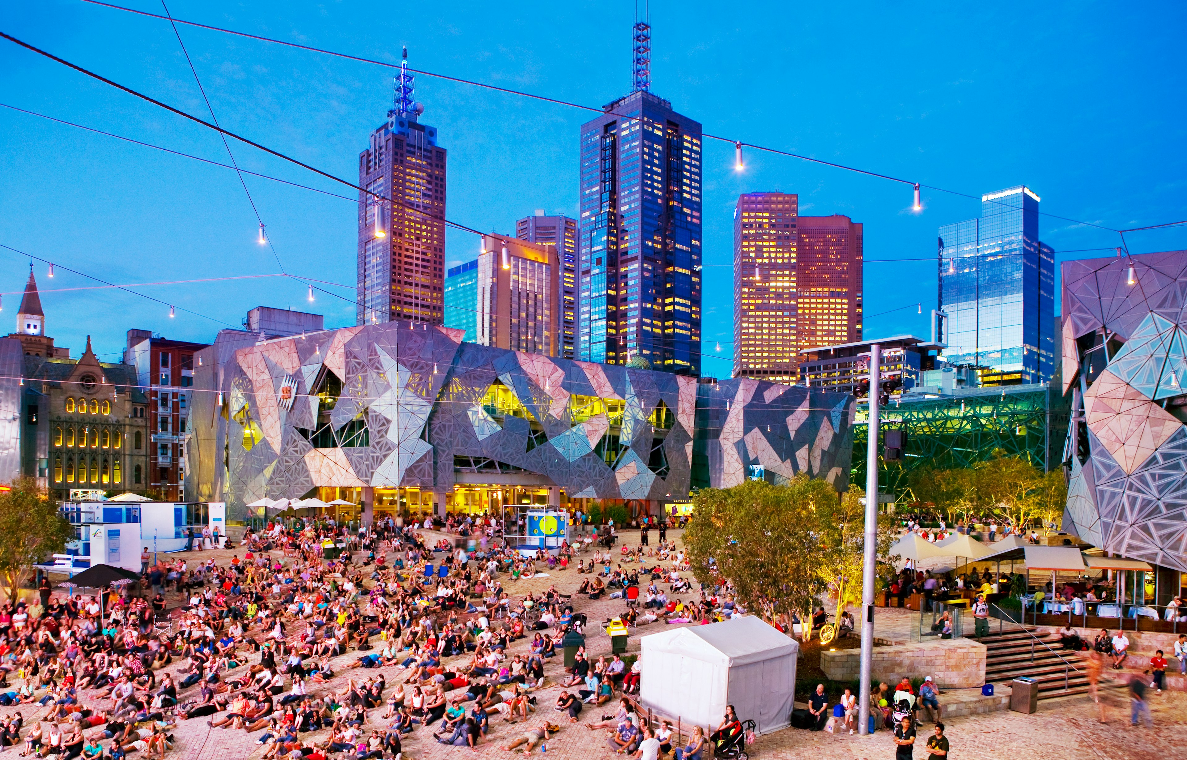 People relax in a city square lit up at dusk