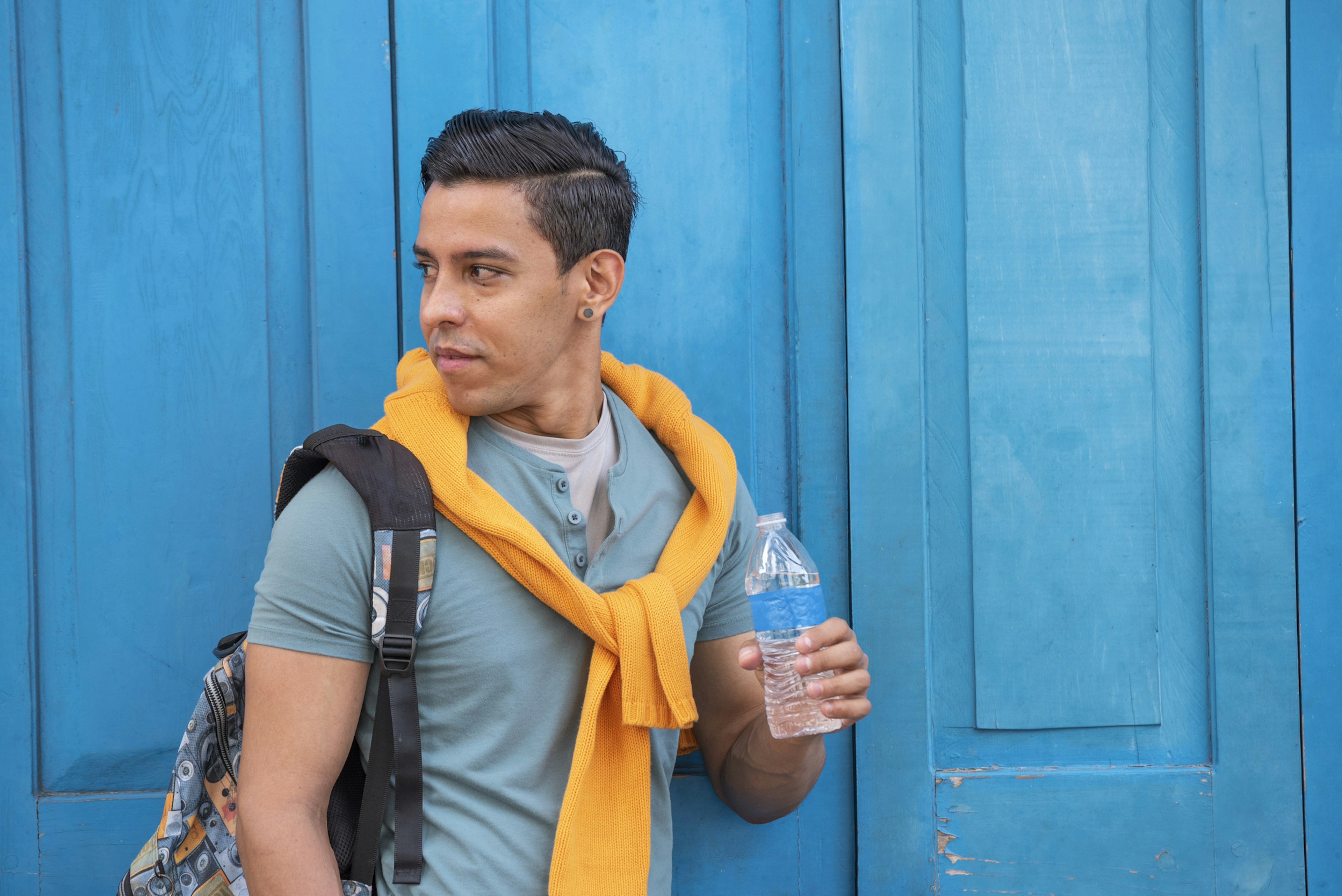 Young hispanic men with a bottle of water standing by a blue door, Panama