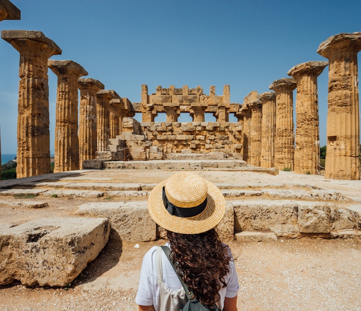 Rear view of a woman with a hat while she's admiring an ancient temple in Sicily. Sunny day. Cool straw hat.
1364745633