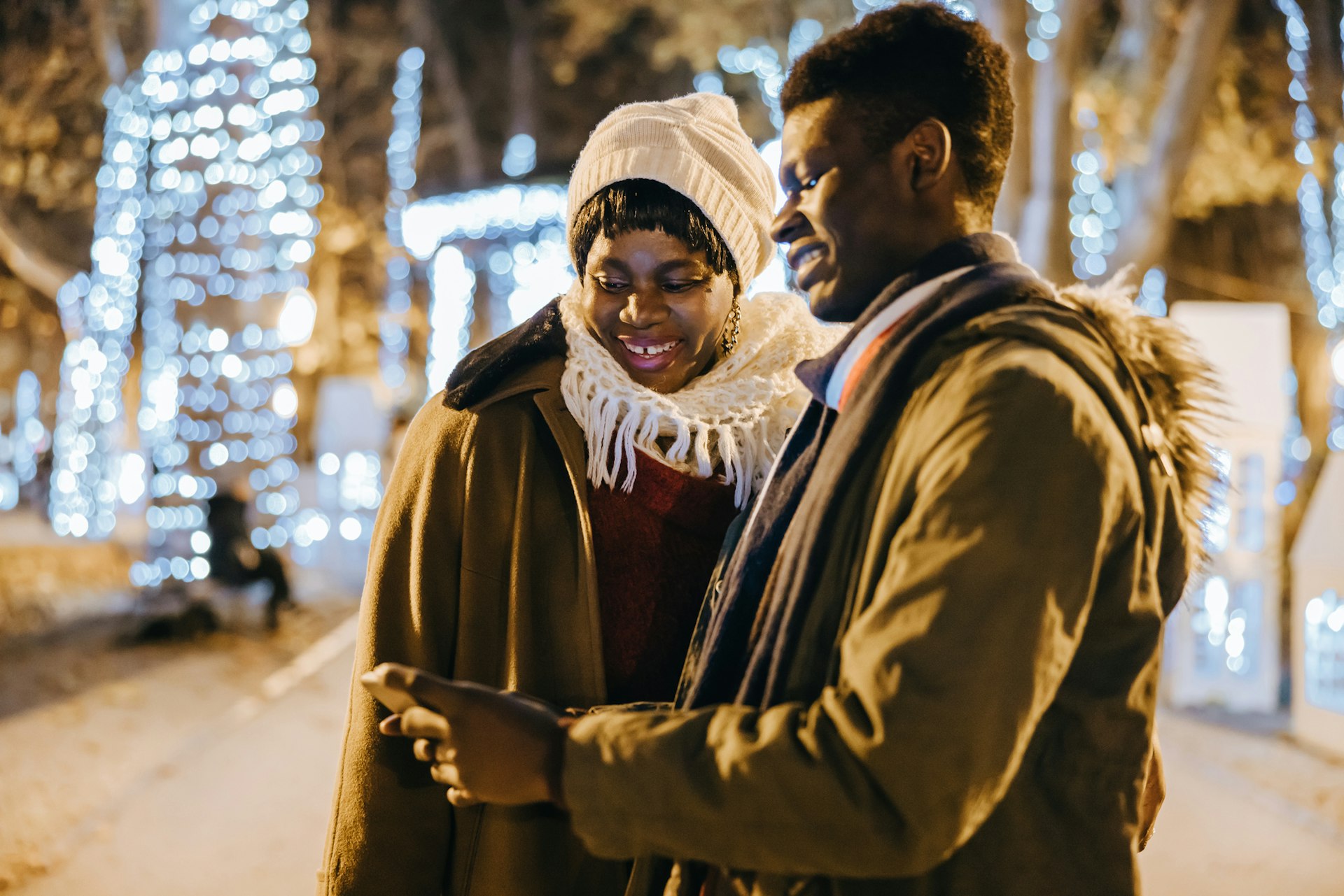 Young African American man showing mobile phone to his mother on street at night in front of a lit up Christmas tree at Zagreb Christmas market
