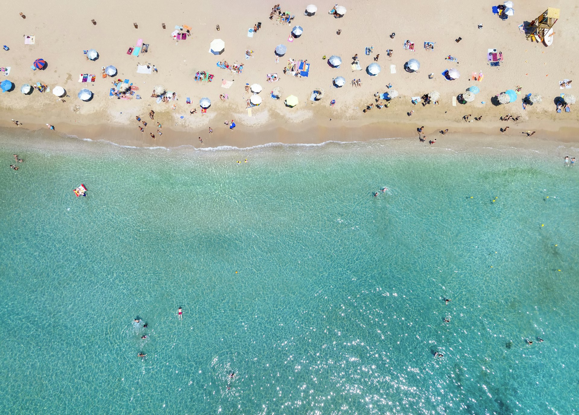 An overhead view of a turquoise sea with people on the beach in Athens, Greece