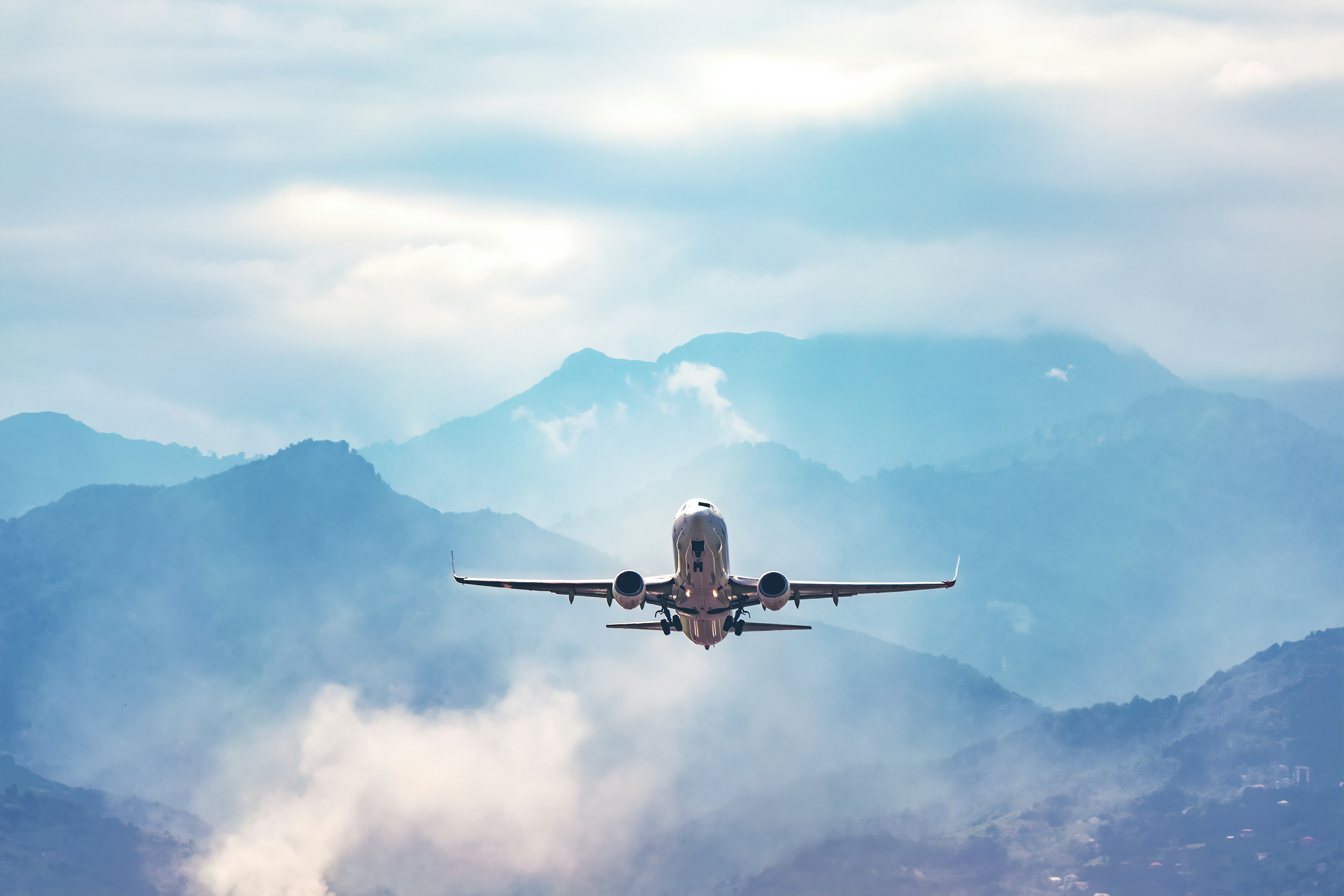 A plane flies above blue misty mountains