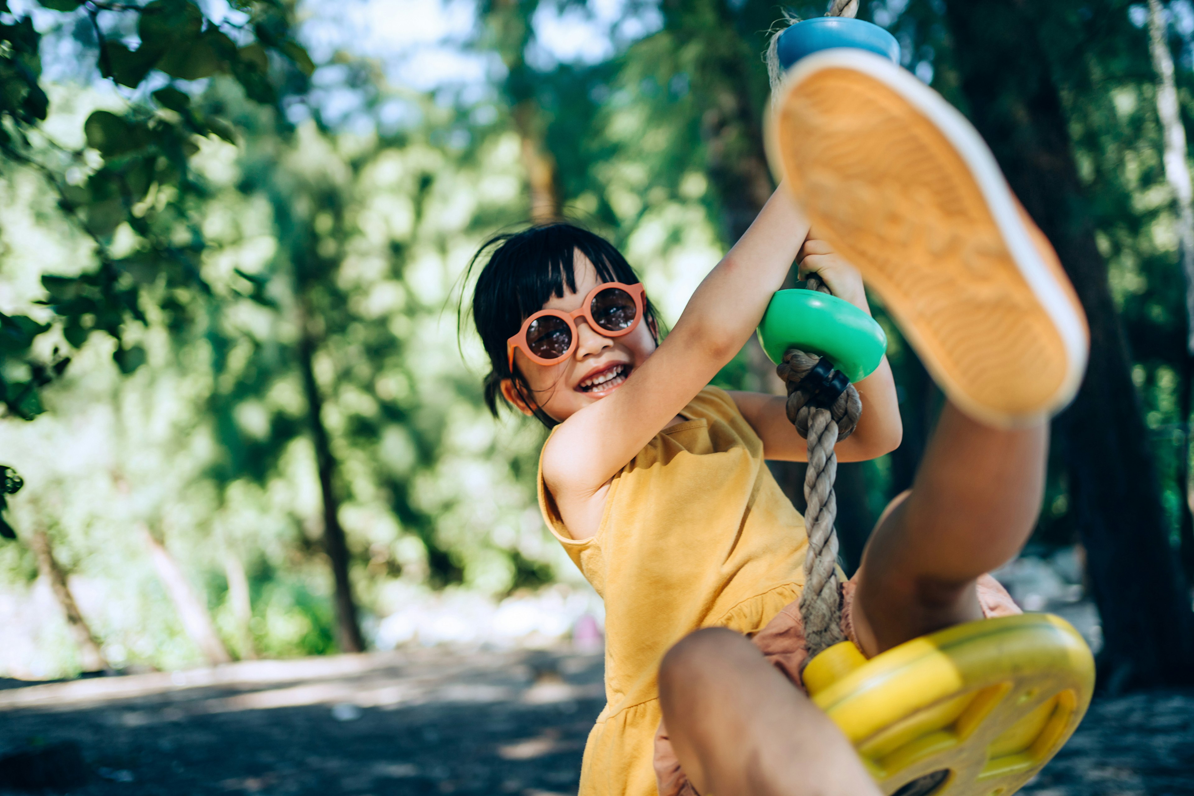 A young girl on a swing in a playground with the sun shining behind her