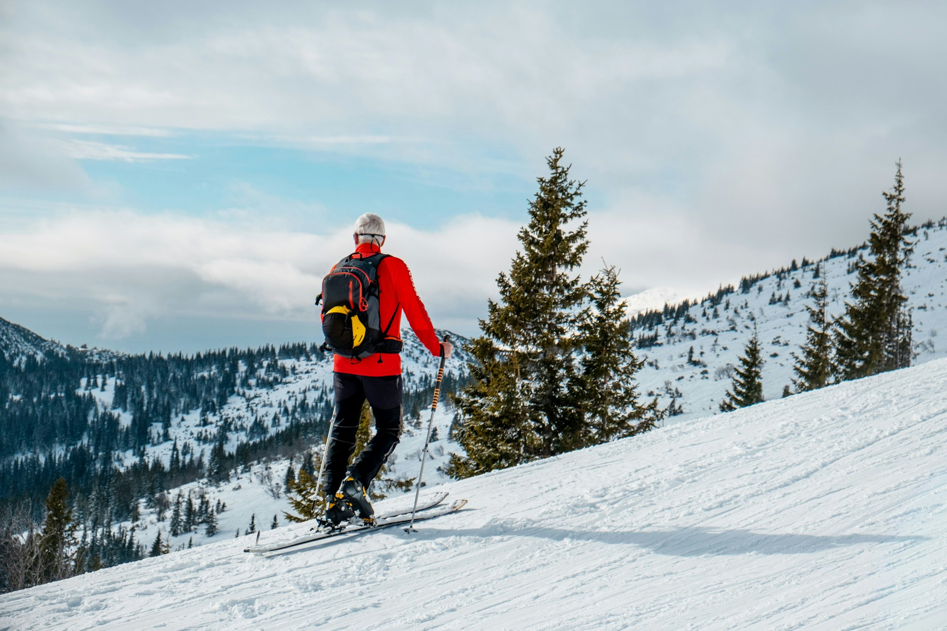 A senior man in ski clothes stands and looks out across the Jasná ski slopes