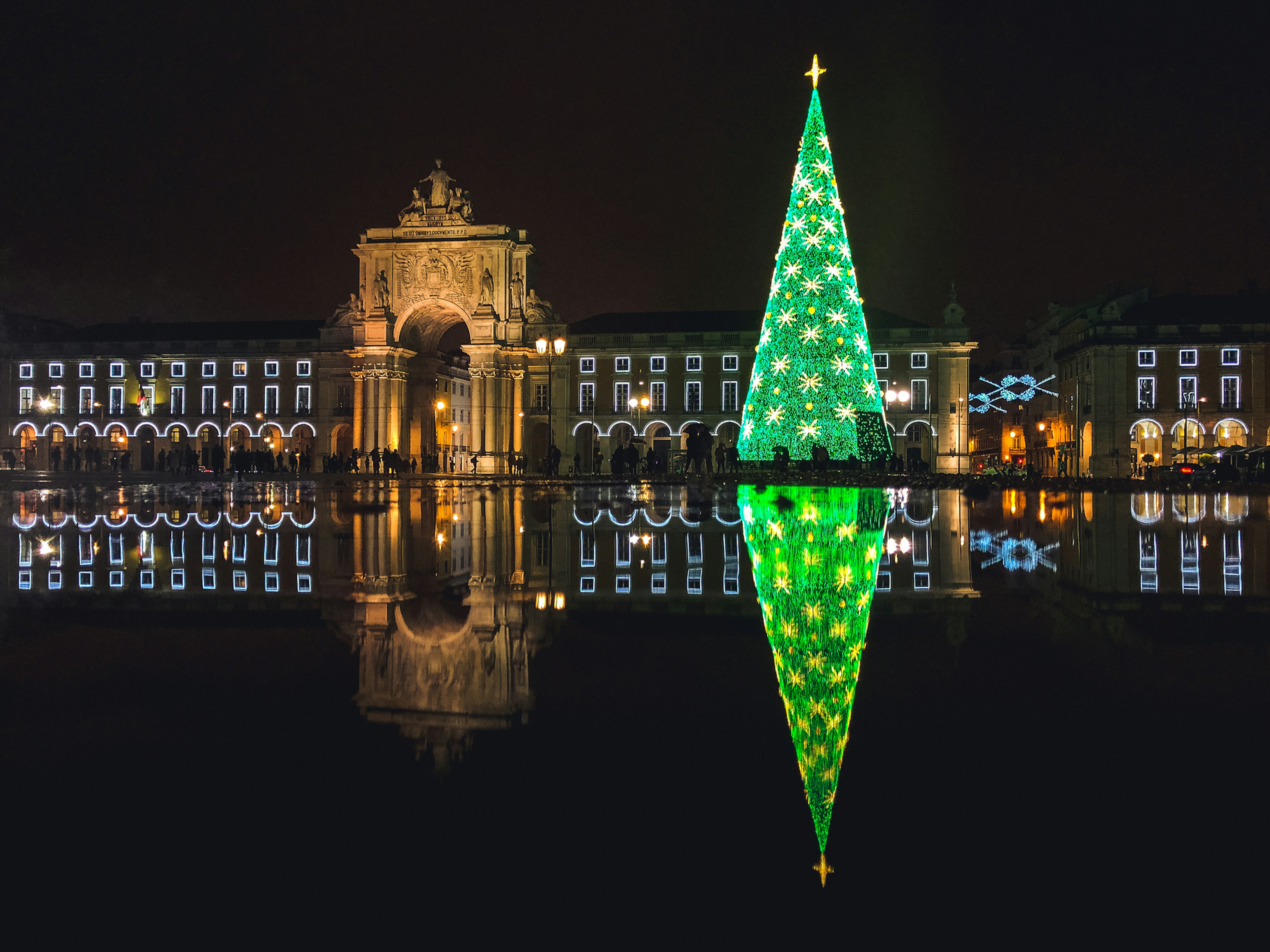 Christmas tree and decorations in Lisbon, Portugal lit up at night. It's almost black, with bright green lights