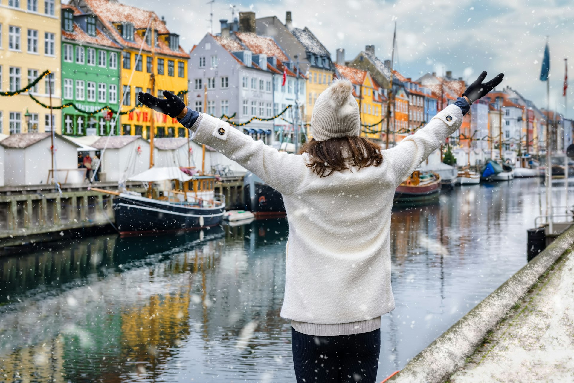 A happy tourist woman enjoys the view to the beautiful Nyhavn area in Copenhagen, Denmark, during winter time with snow and Christmas decorations